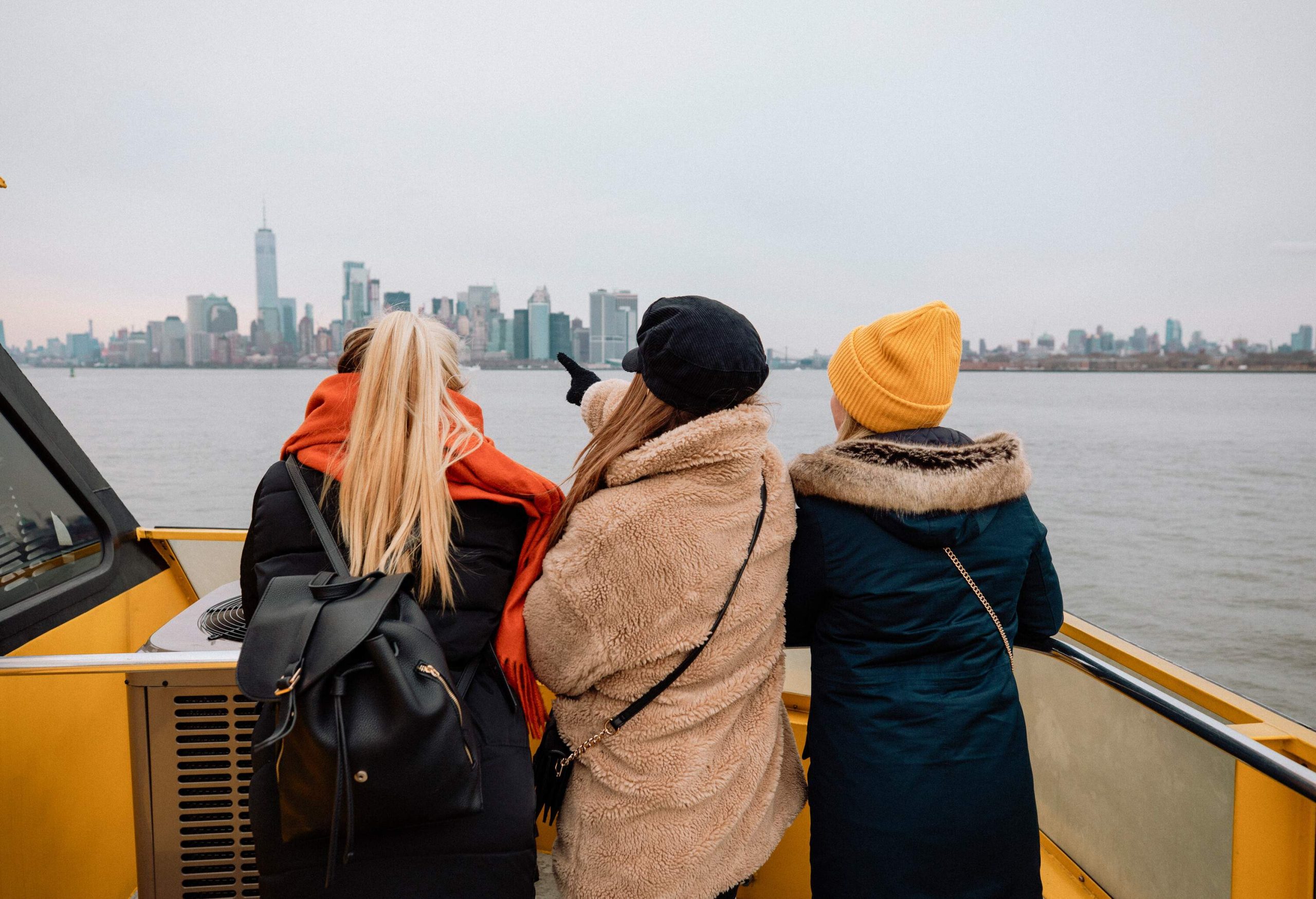 Three friends in winter clothes enjoy the views of a cityscape from a tour boat.