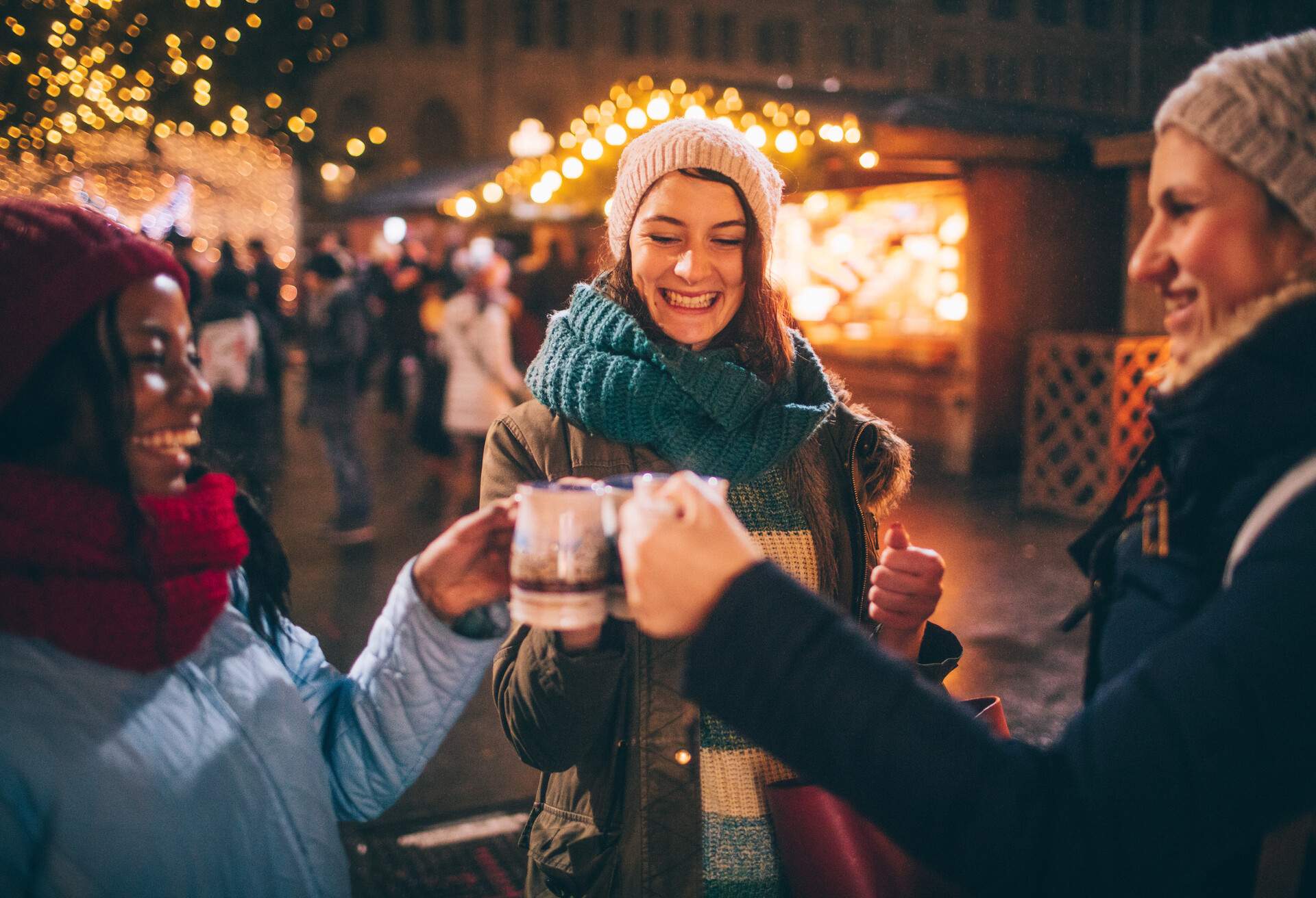 Three women in winter clothes raising their cups cheerfully.