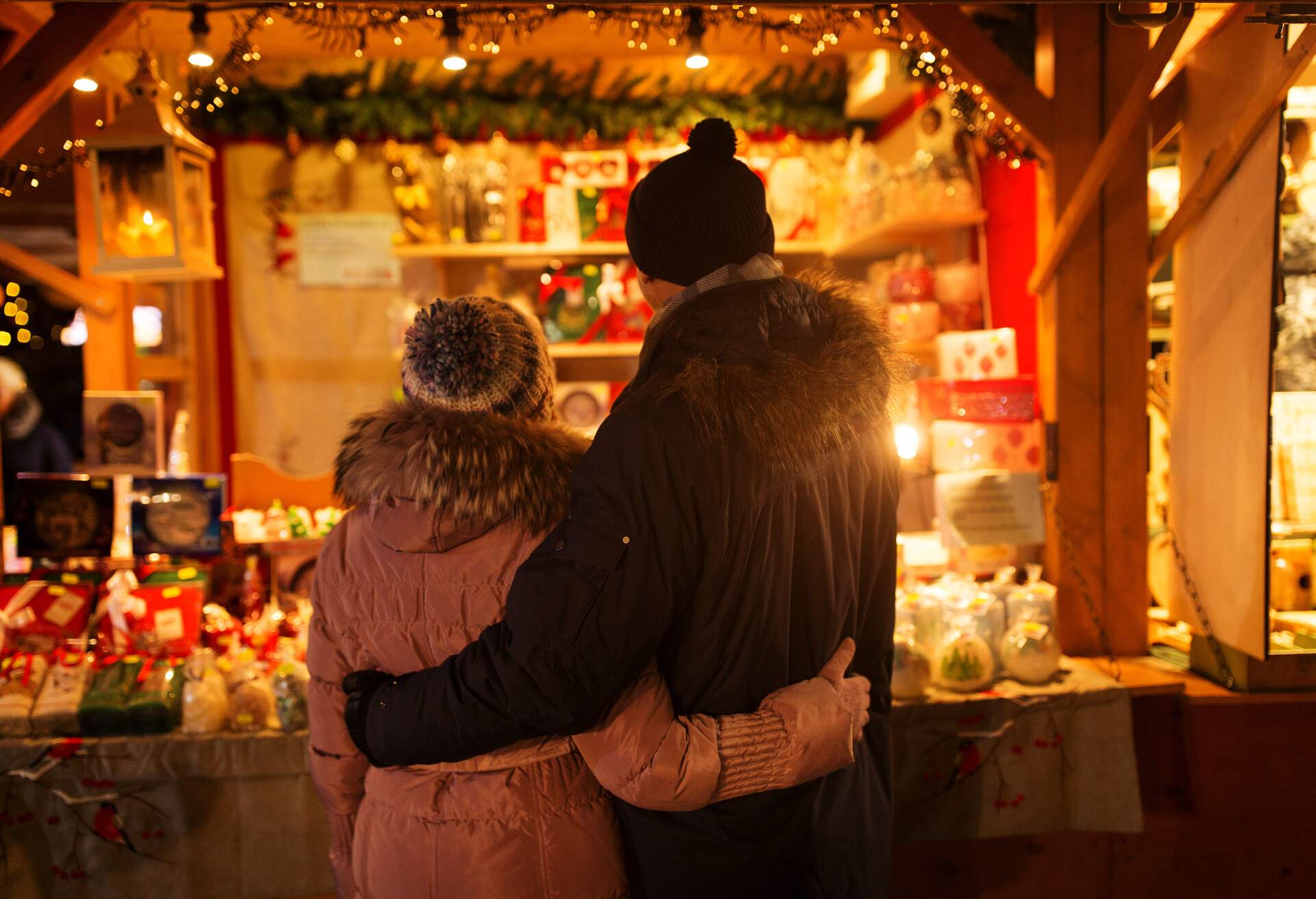 Couple in winter coats holding each other's backs as they look at a Christmas shop.