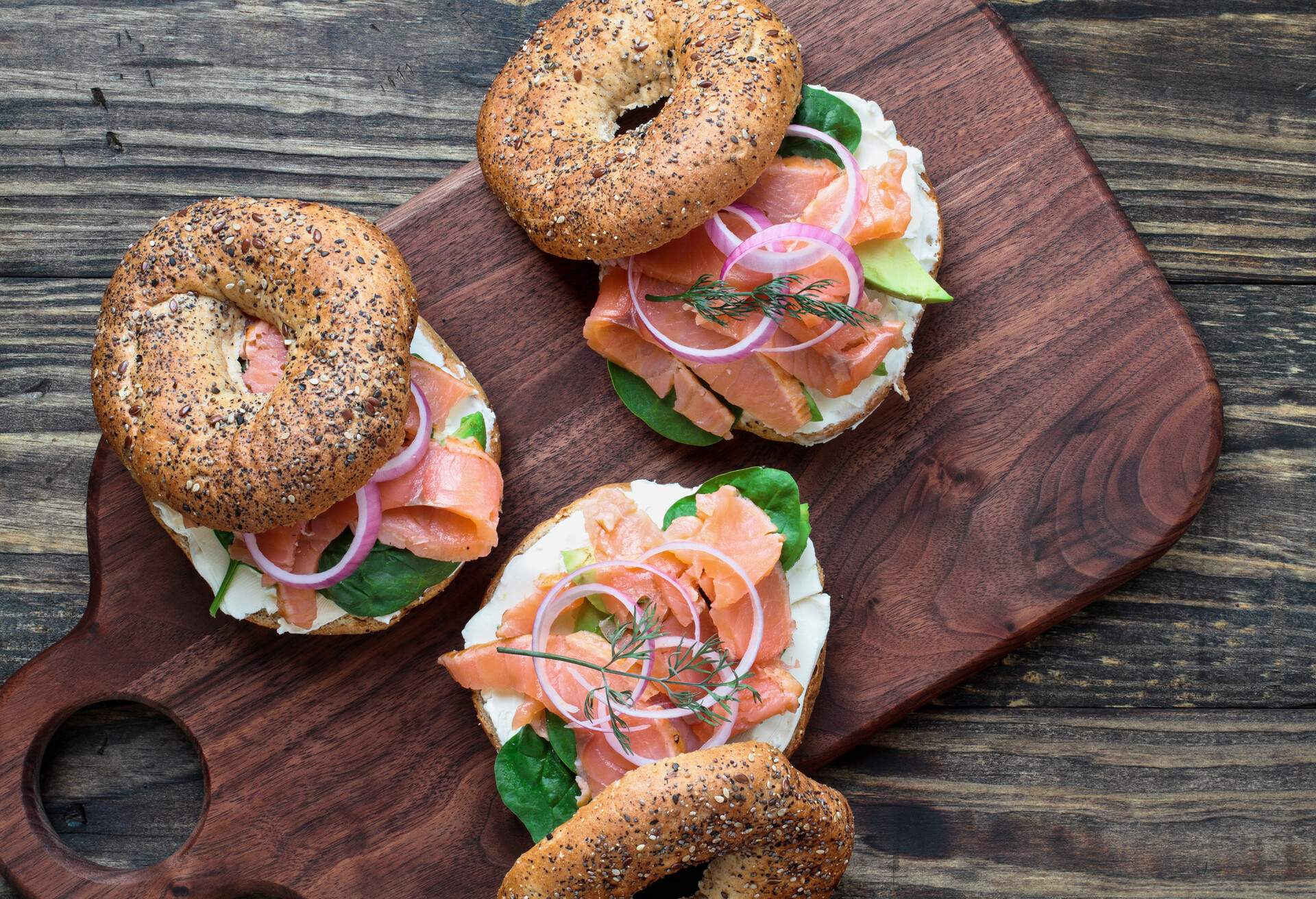 Lox - Everything bagel with smoked salmon, spinach, red onions, avocado and cream cheese over a rustic wood table background. Image shot from top view or flat lay position.