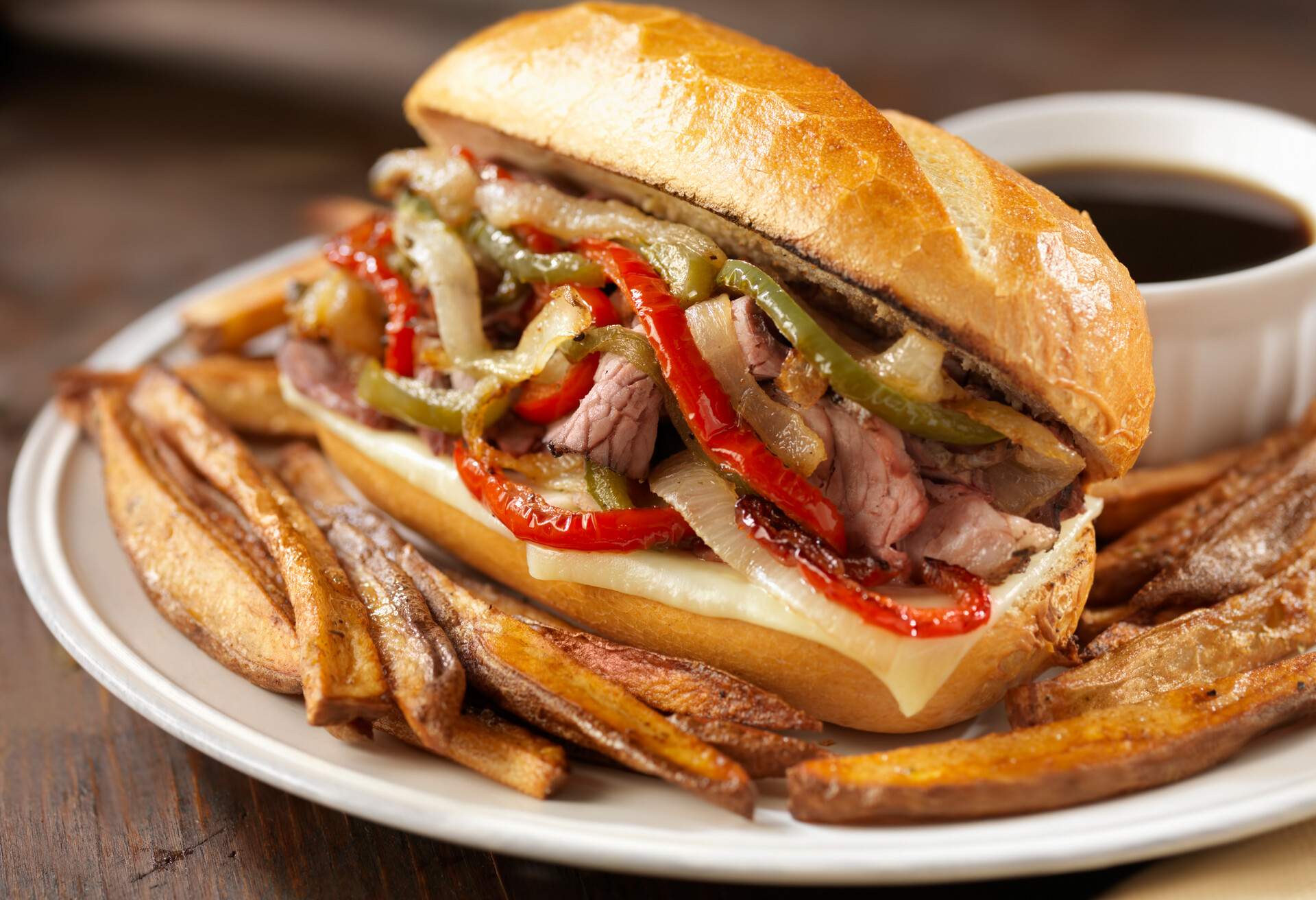 Philly Prime Rib Sandwich with Roasted Onions, Peppers and Melted Cheese on a Toasted Crusty French Roll with French Fries and Au Jus -Photographed on Hasselblad H3D2-39mb Camera