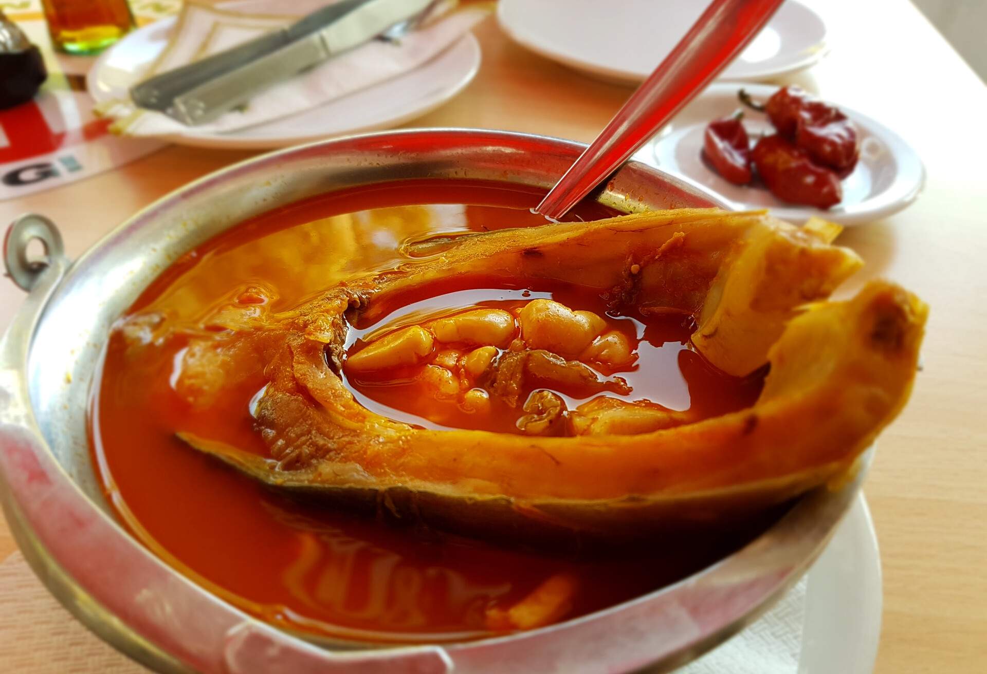A red fish soup topped with fish fillet served in a metal soup bowl.