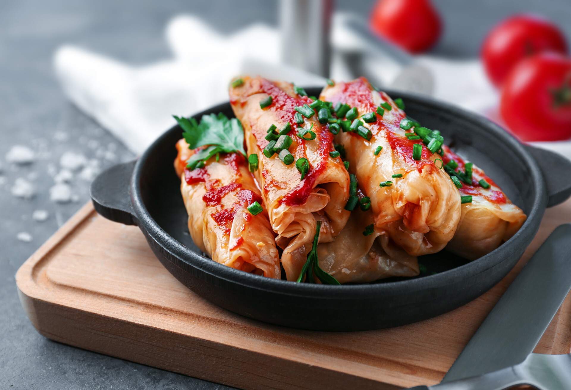 Pan with stuffed cabbage leaves in tomato sauce on wooden board