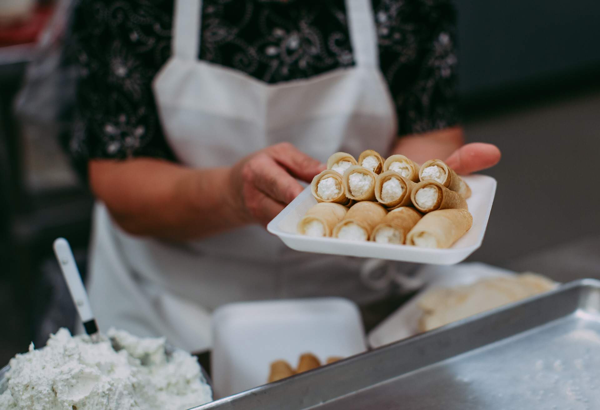 Photo of a person with an apron holding a tray of freshly made Ukrainian Nalesniki.