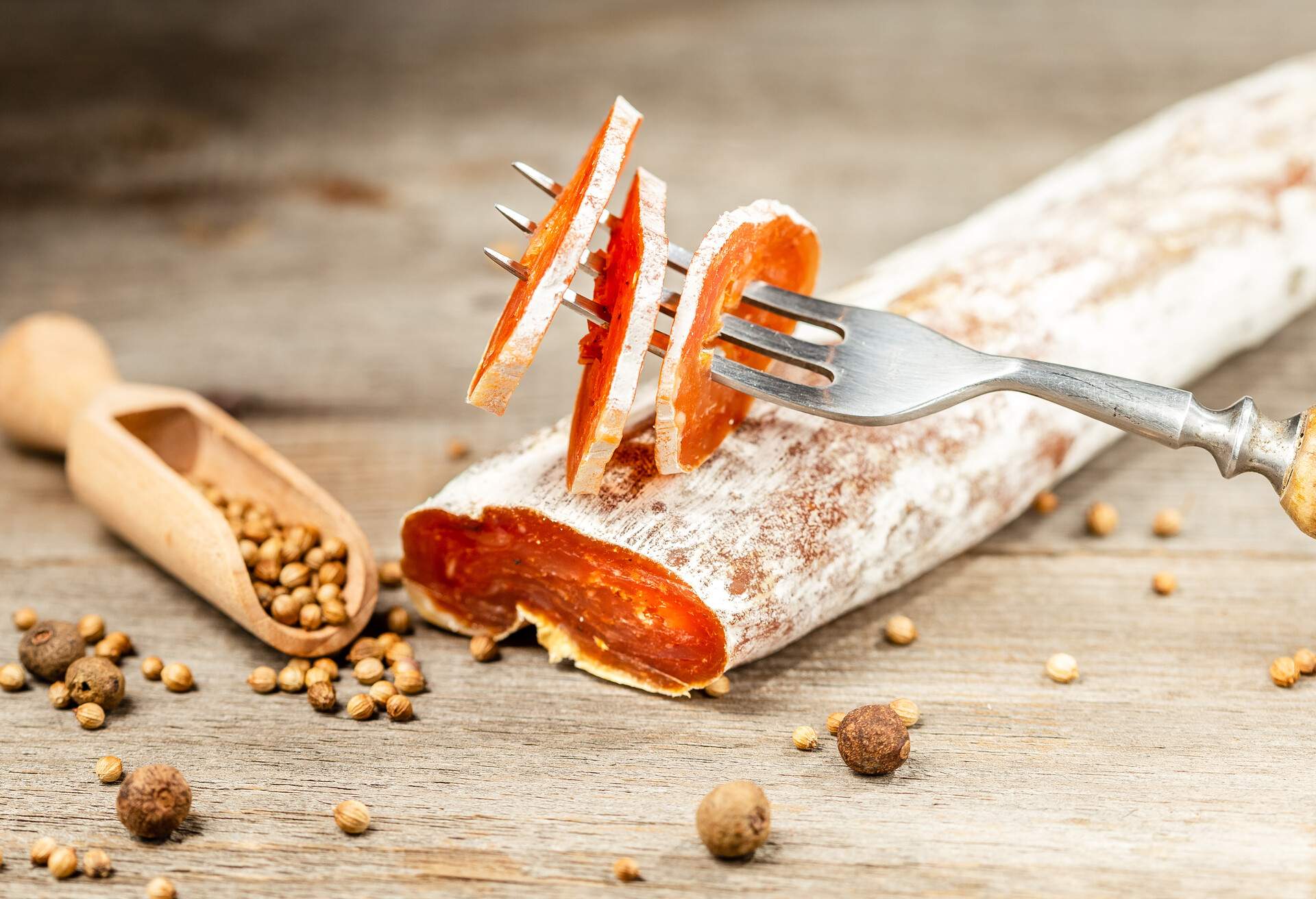 Smoked Chicken meat Sausage covered with edible penicillin mold sliced on the fork and pepper seeds on the wooden table