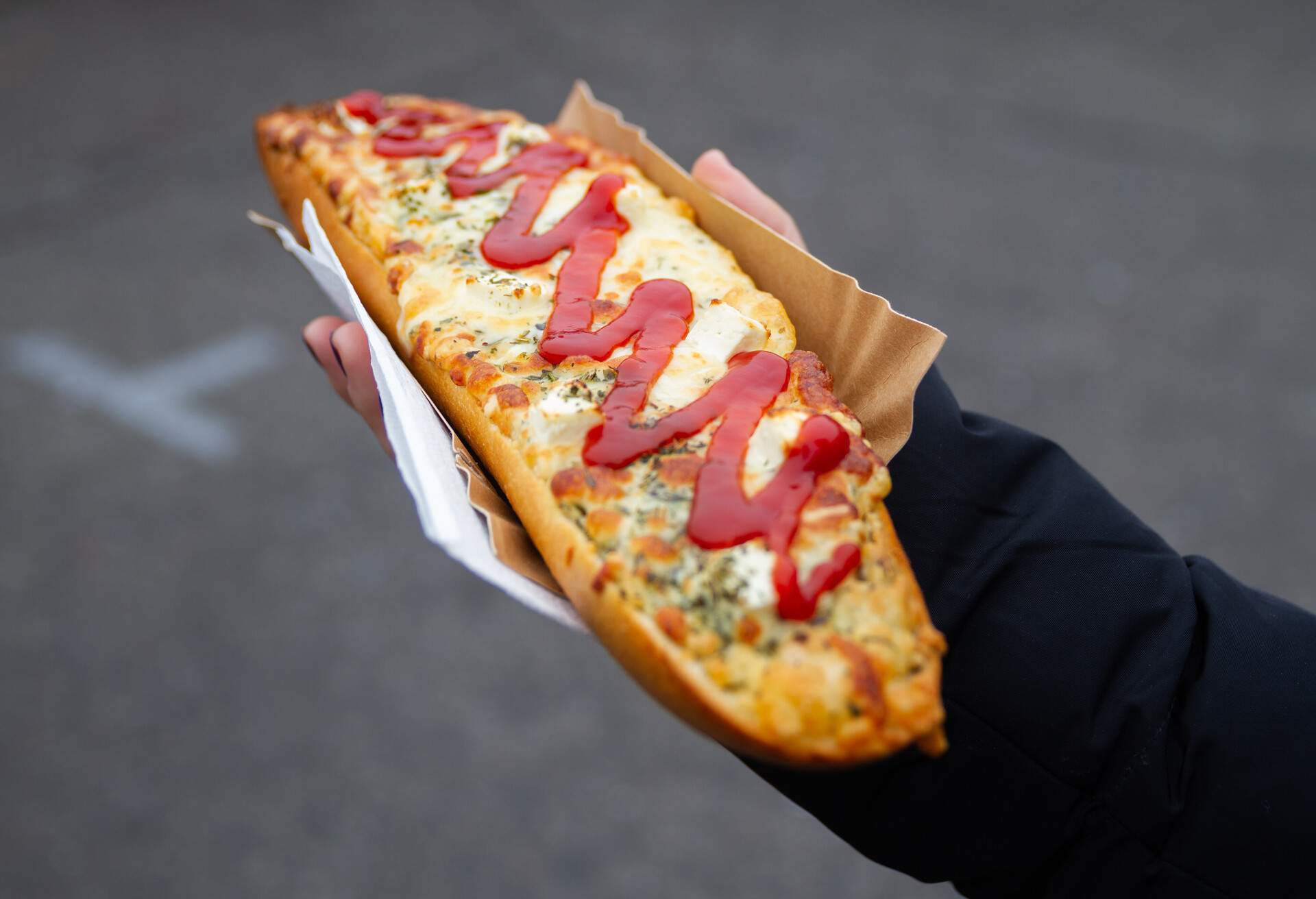 Female hand holding delicious sandwich called Zapiekanka near the Okraglak street food court on Plac Nowy (Jewish Square). Famous Zapiekanki Krakowskie in Kazimierz district of Old Town Krakow, Poland.