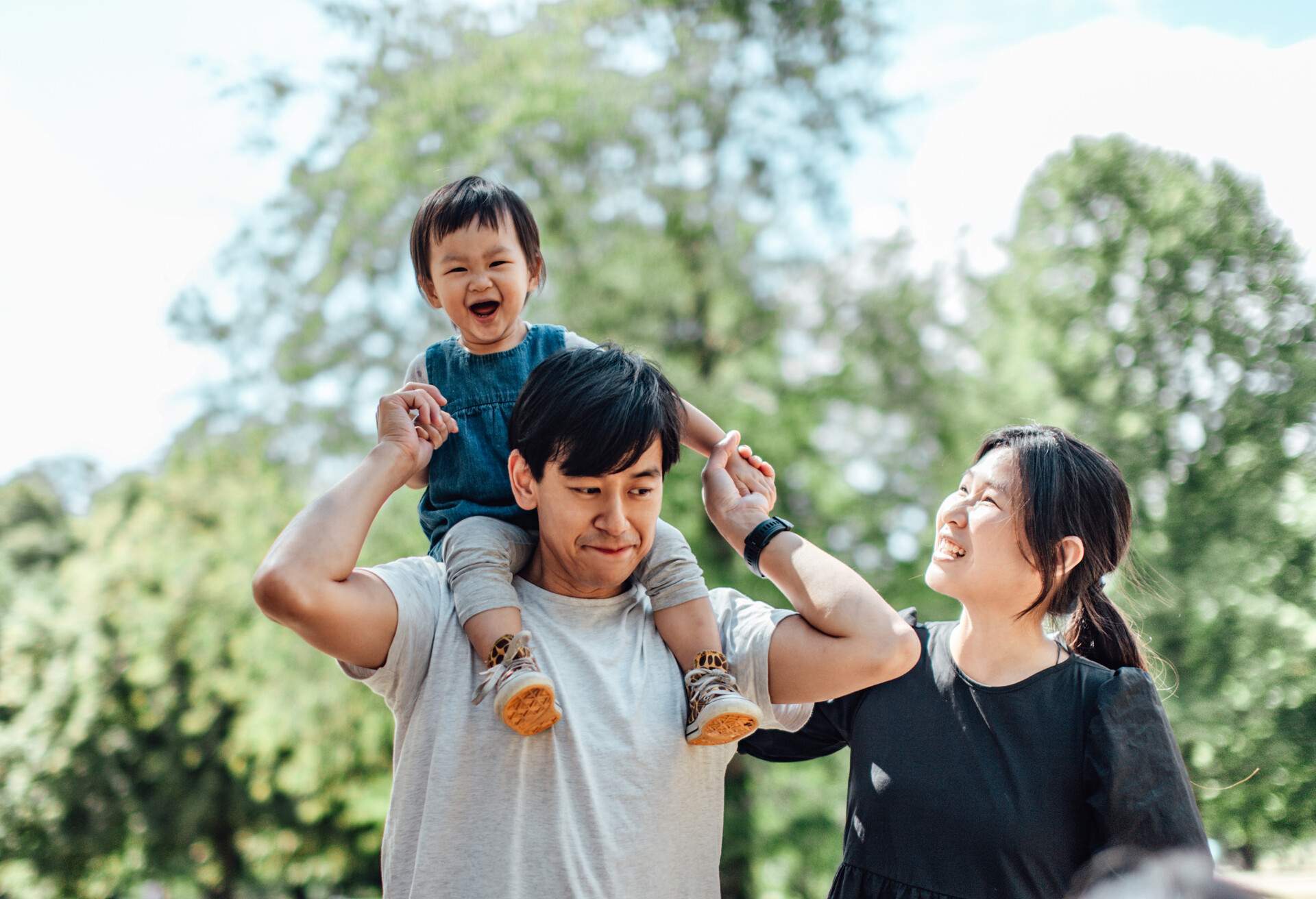 Happy young Asian family having a great time in the park on a sunny day. They are having fun and smiling joyfully.