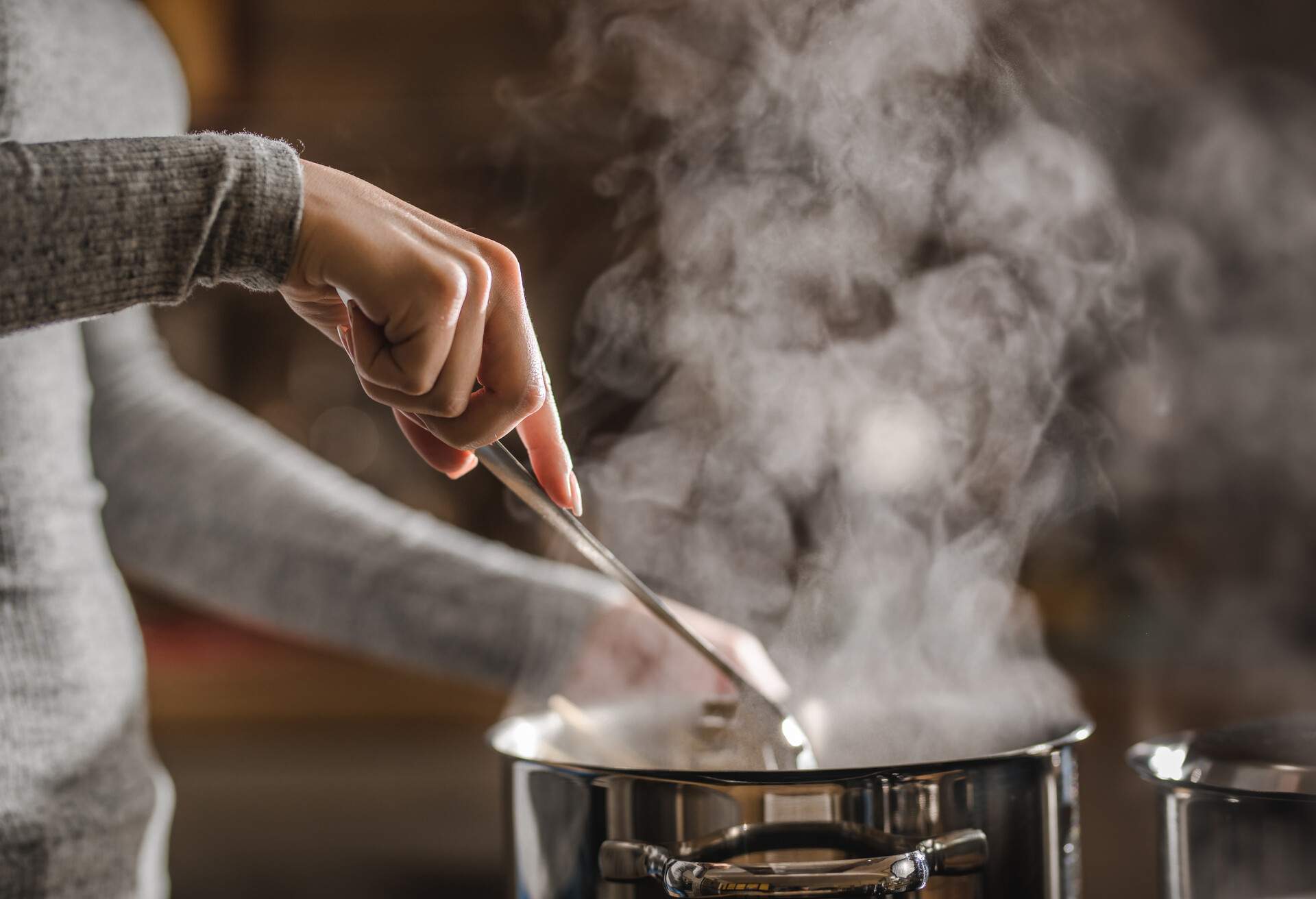 Unrecognizable woman stirring soup in a saucepan while making lunch.