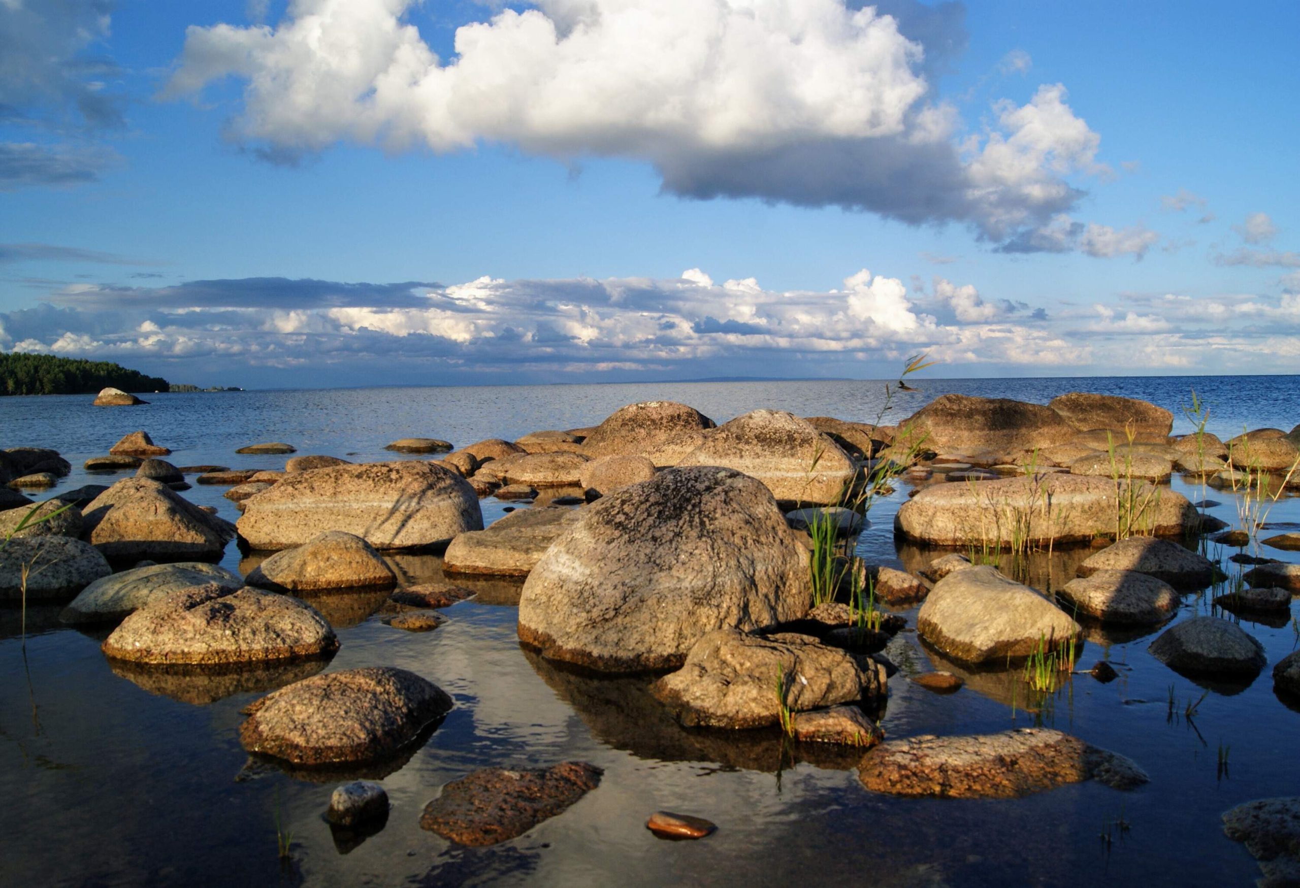 Large boulders on the shore of a beach under the cloudy blue sky.