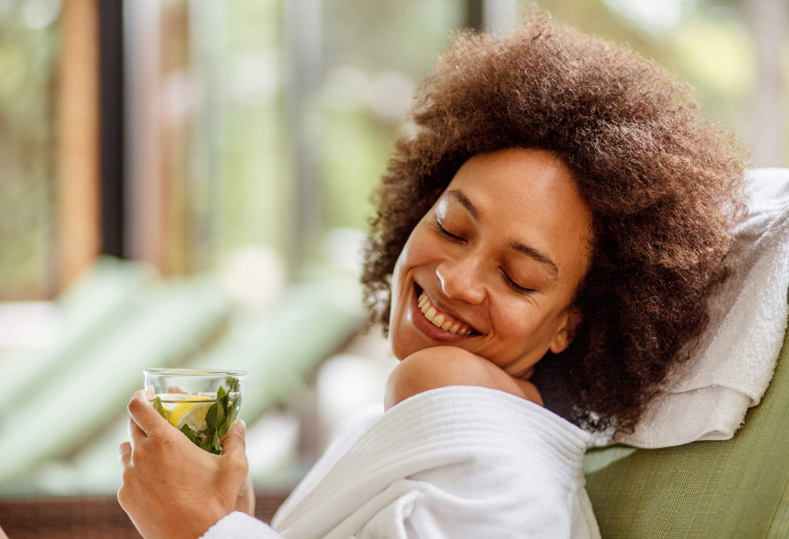 Smiling young woman relaxing in a cozy bathrobe while enjoying a refreshing herbal tea on her weekend getaway at the wellness resort