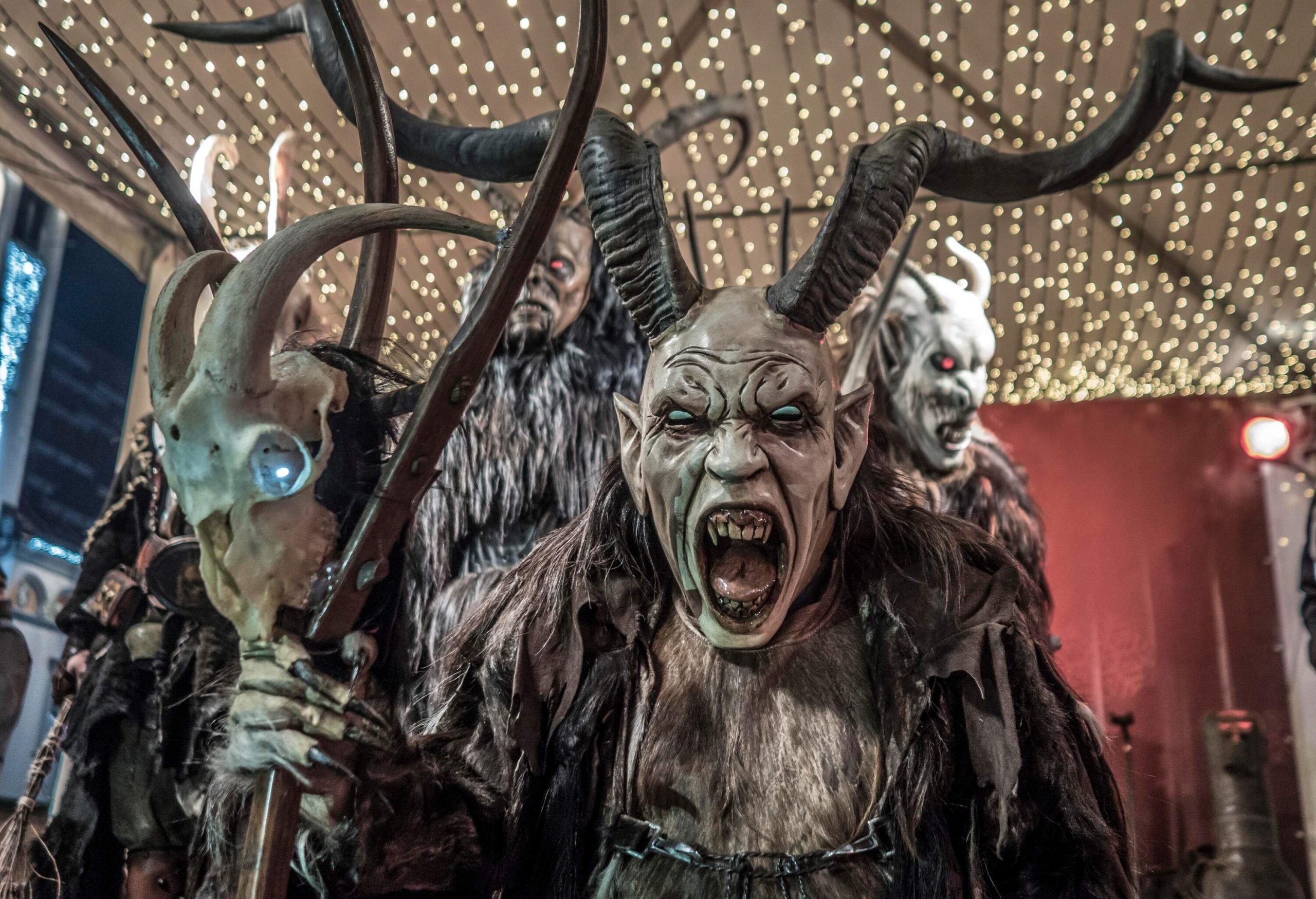 A statue of Krampus and other horned figures under a canopy of string lights.