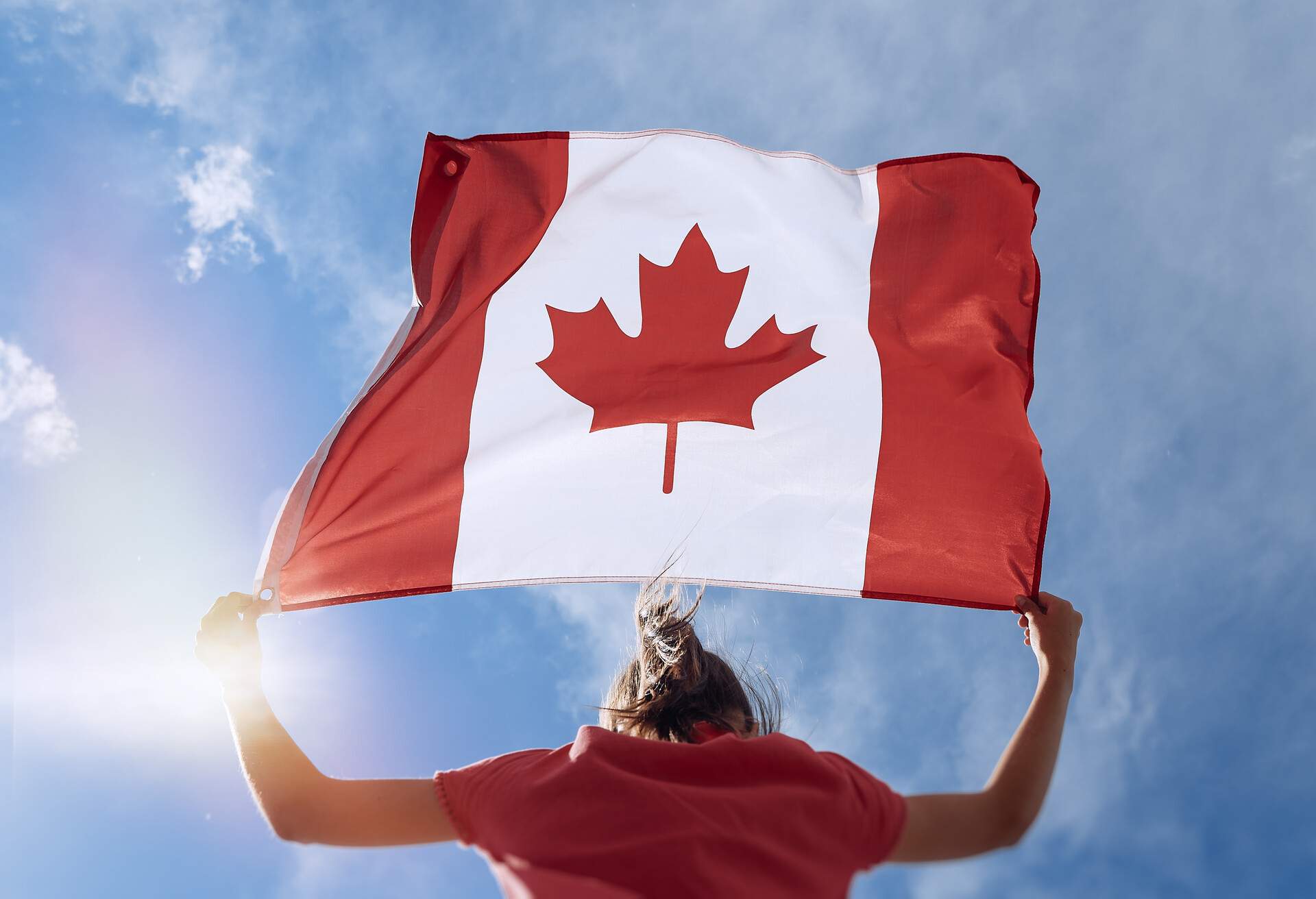 Child girl is waving Canadian flag on top of mountain at sky background