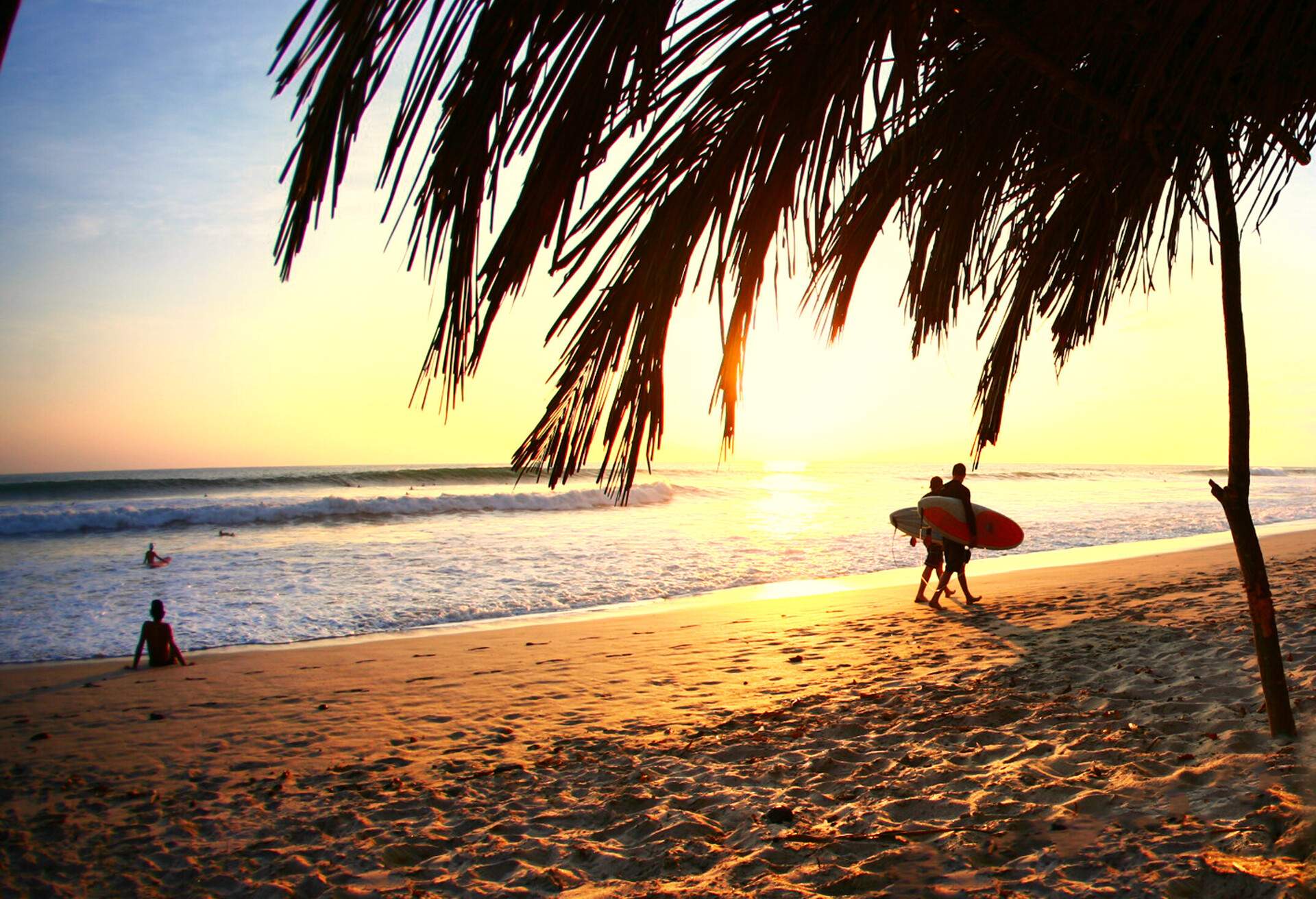 Two male surfers walking home on beach during sunset on Playa Santa Teresa, Costa Rica.