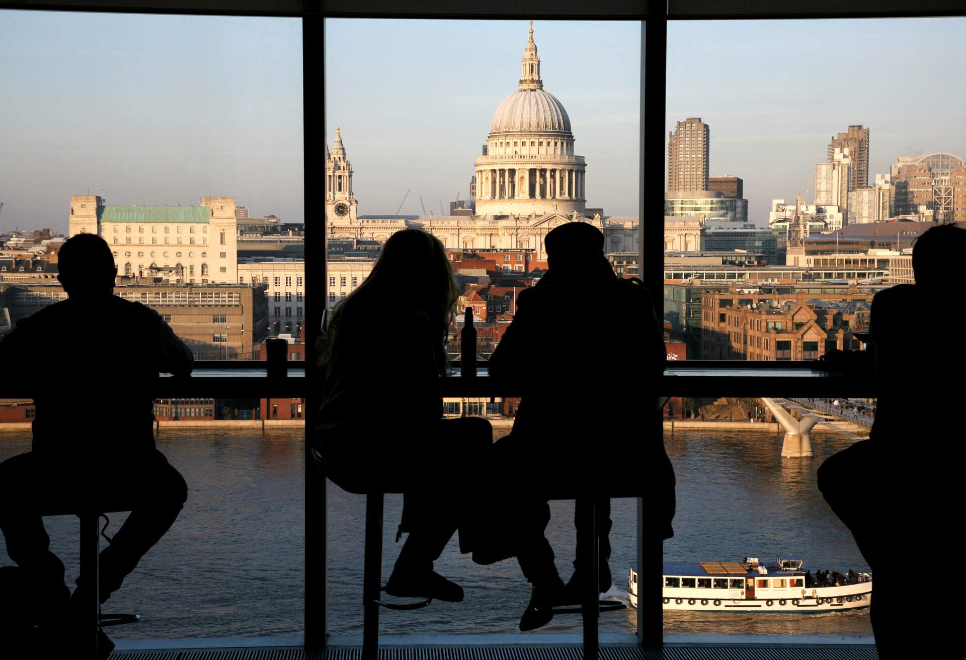 Silhouette of people sitting on window seat overlooking a dome church and a cityscape along a river.