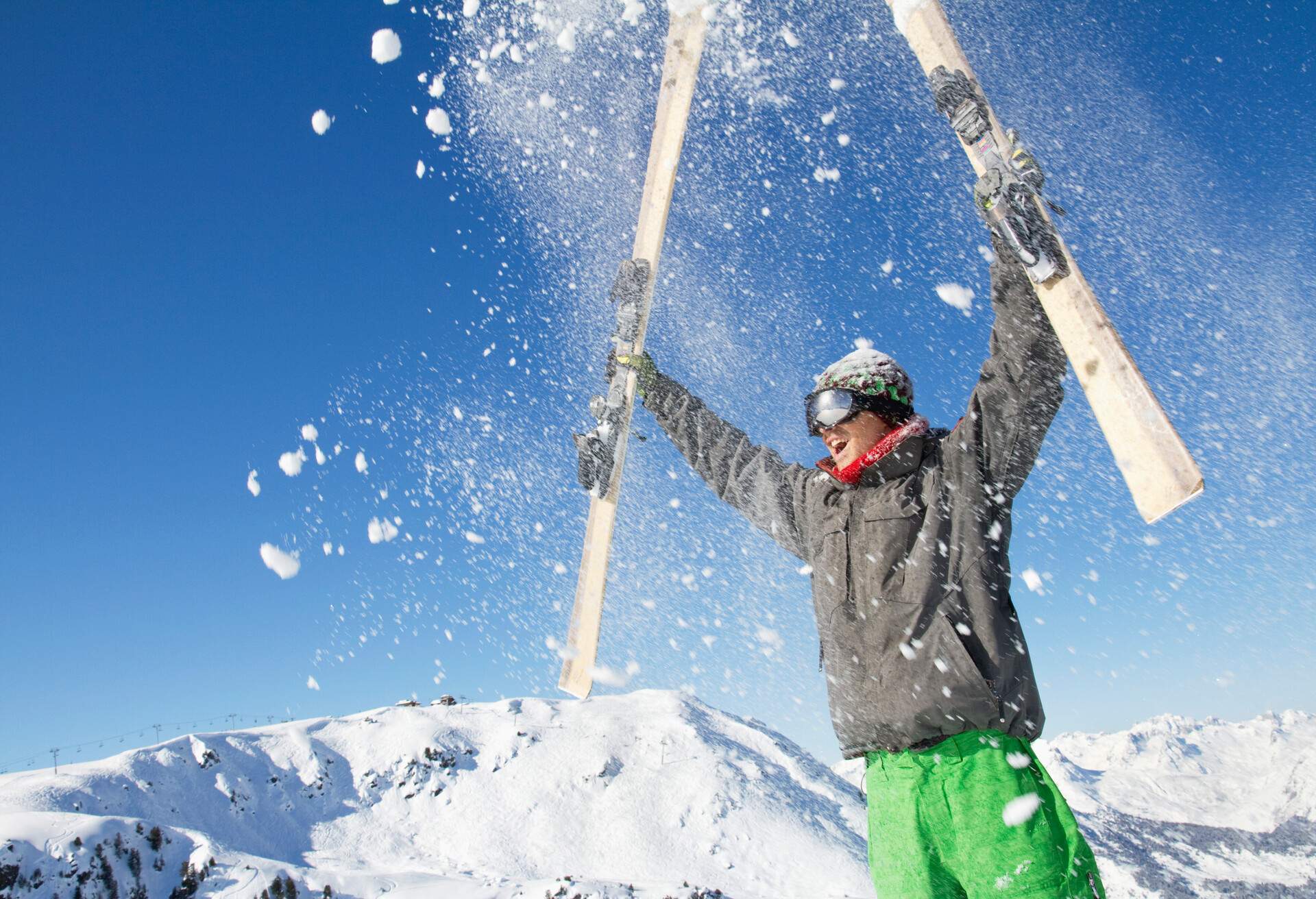 A man dressed for winter raising his ski in the air, causing the snow to spray all around.