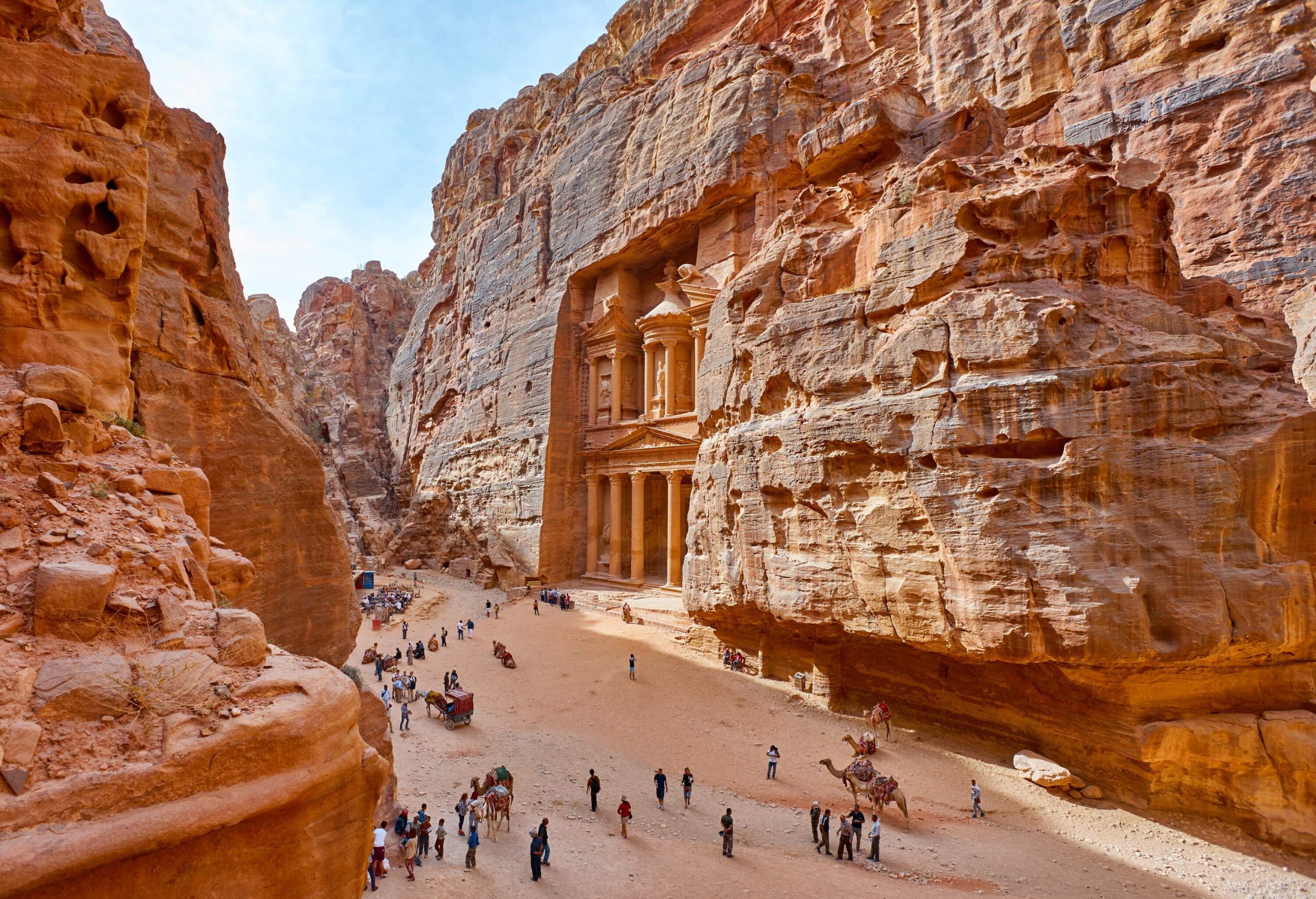A crowded path towards a pillared temple carved on the side of a sandstone cliff.