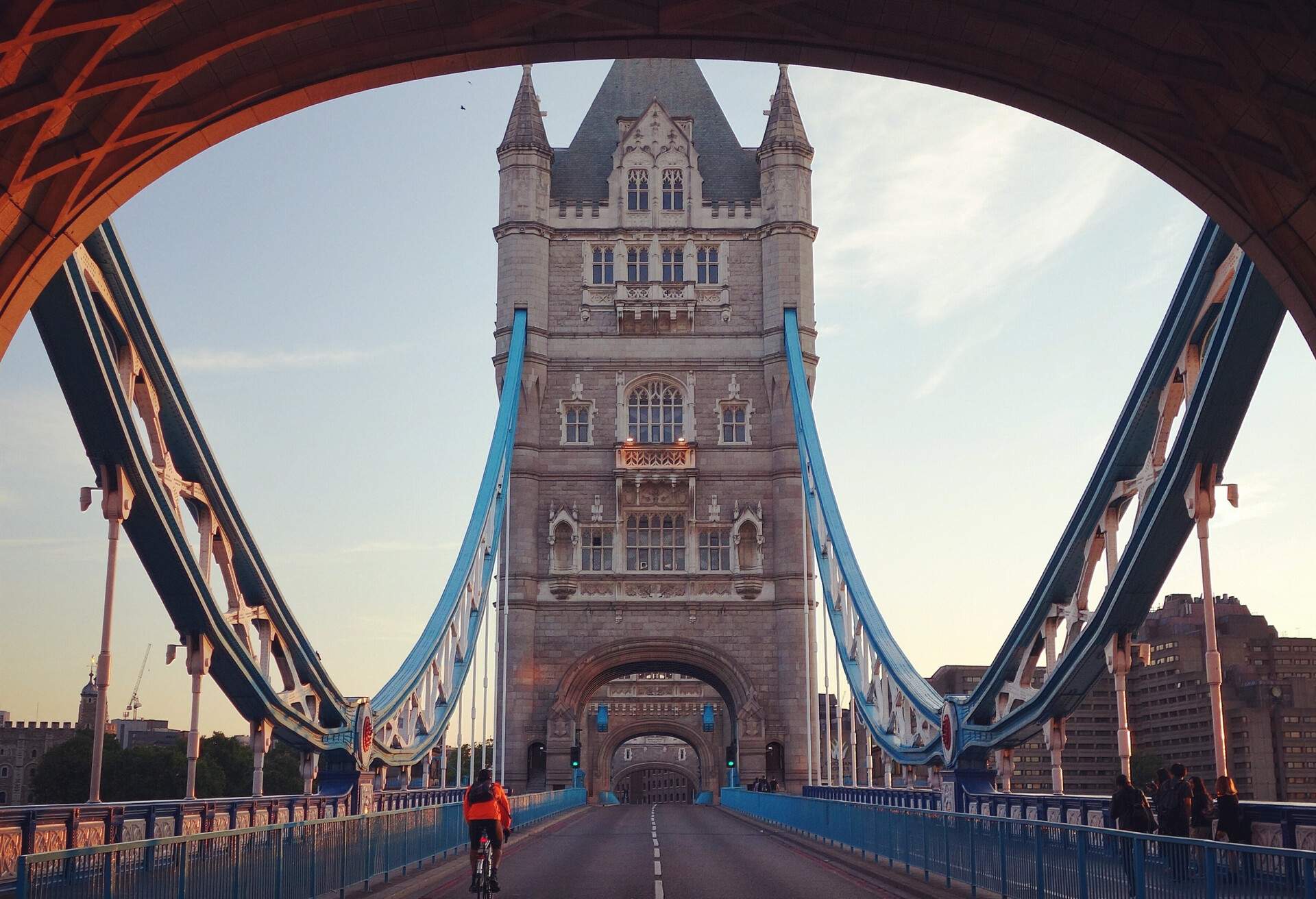 A man wearing an orange pullover riding his bicycle through the Tower Bridge.