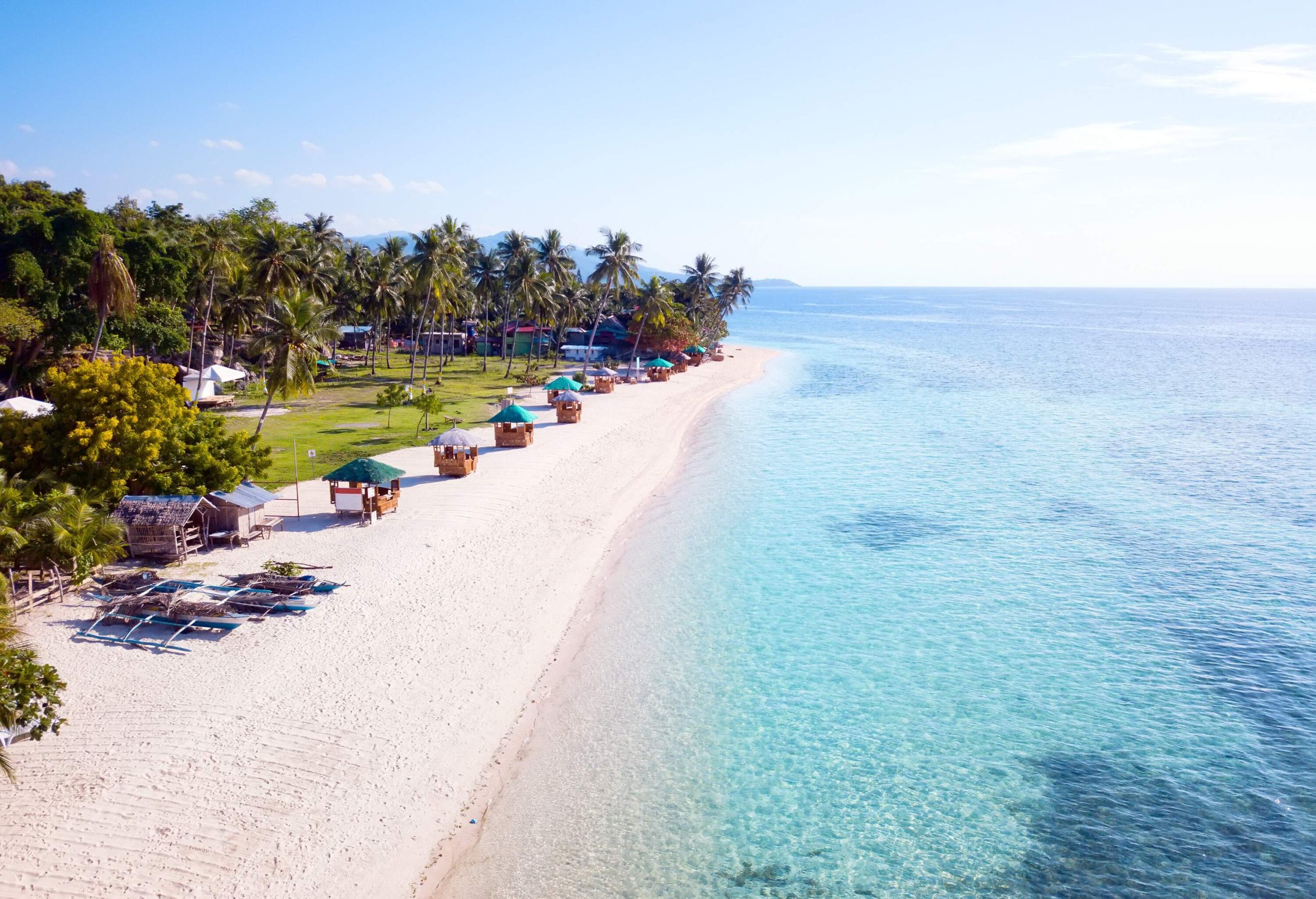 A white sand beach stretching ahead, adorned with charming huts and swaying tropical trees.