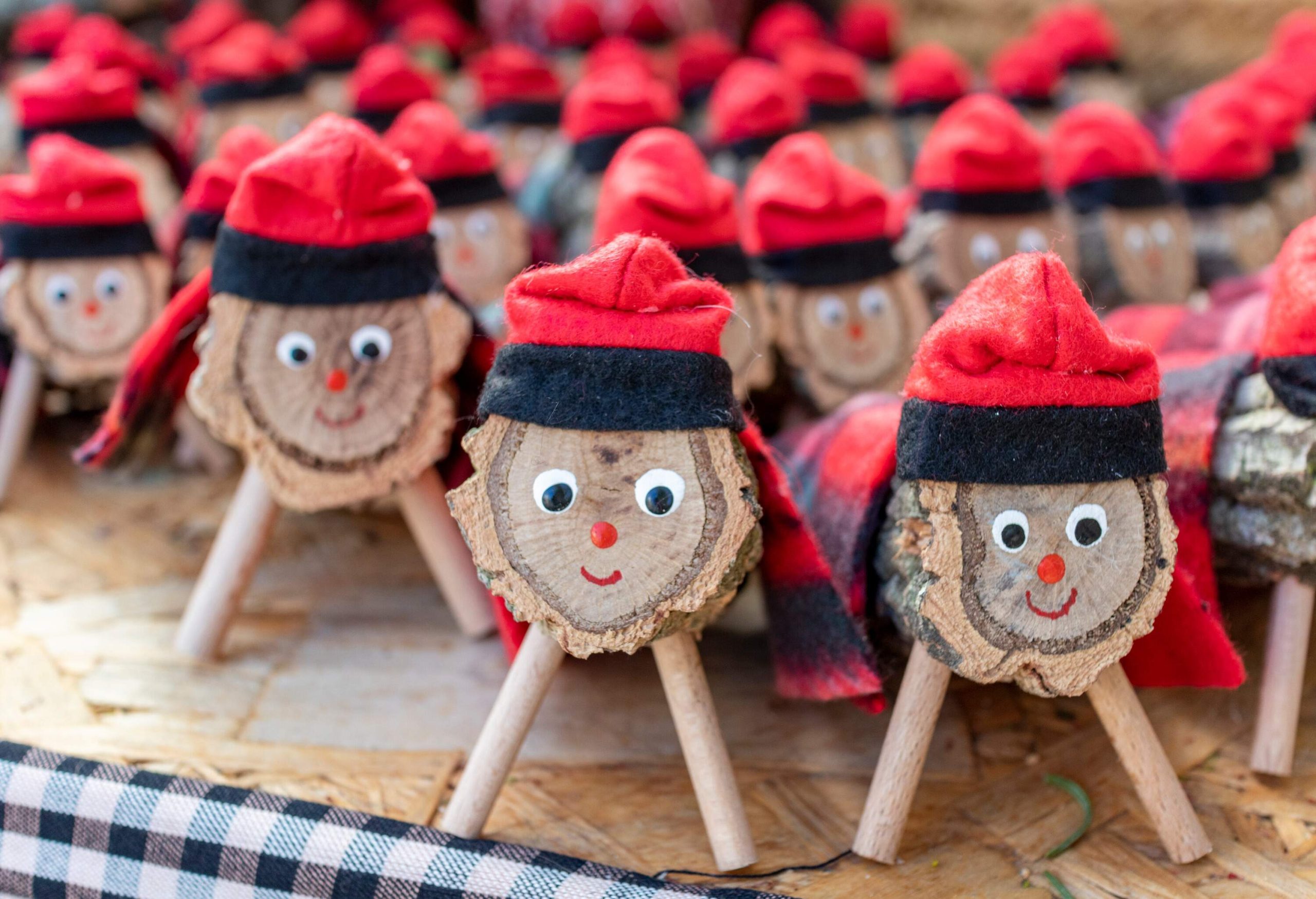 A bunch of chopped tree trunks placed on two sticks with a smiley face wearing a red cap.