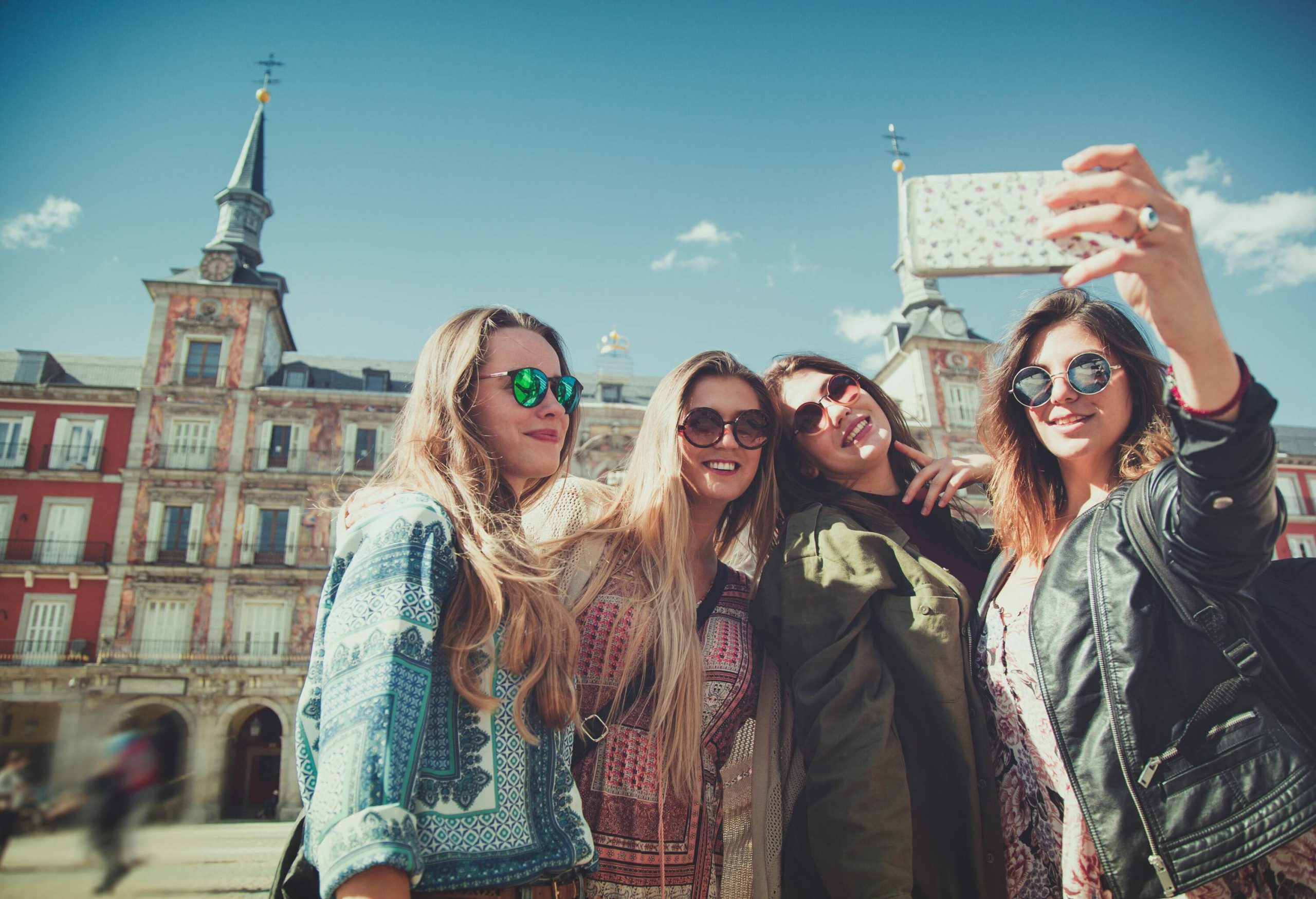 Four women take a selfie in front of a classic historical building.