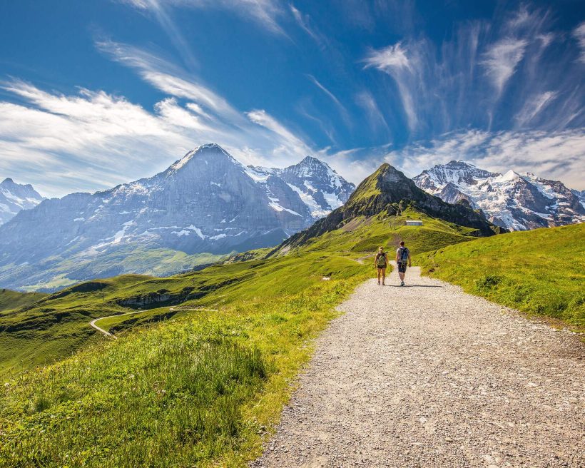 Young couple hiking in panorama trail leading to Kleine Scheidegg from Mannlichen with Eiger, Monch and Jungfrau mountain (Swiss Alps) in the background, Berner Oberland, Grindelwald, Switzerland