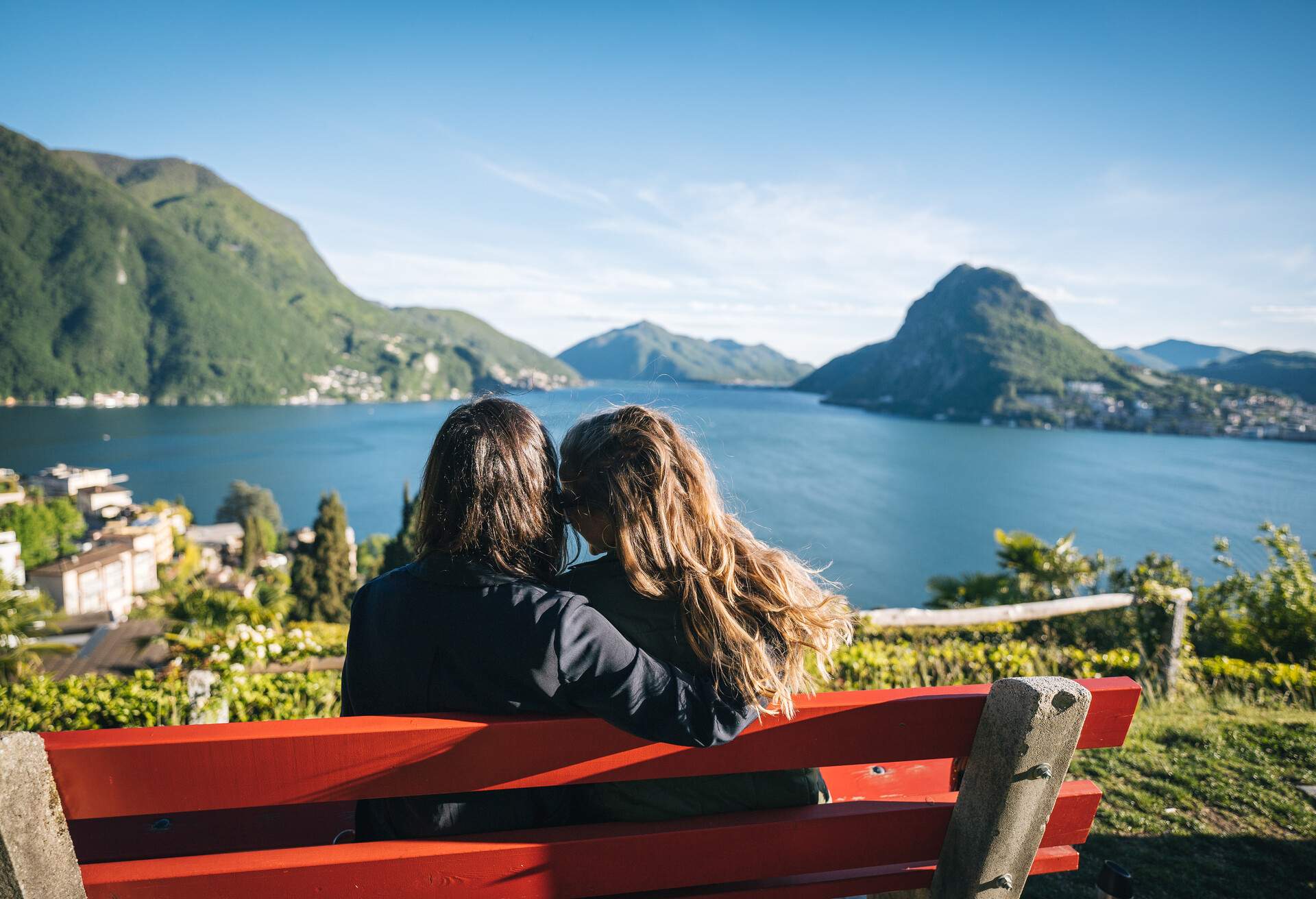 They embrace and look off to coastline of Lake Lugano behind