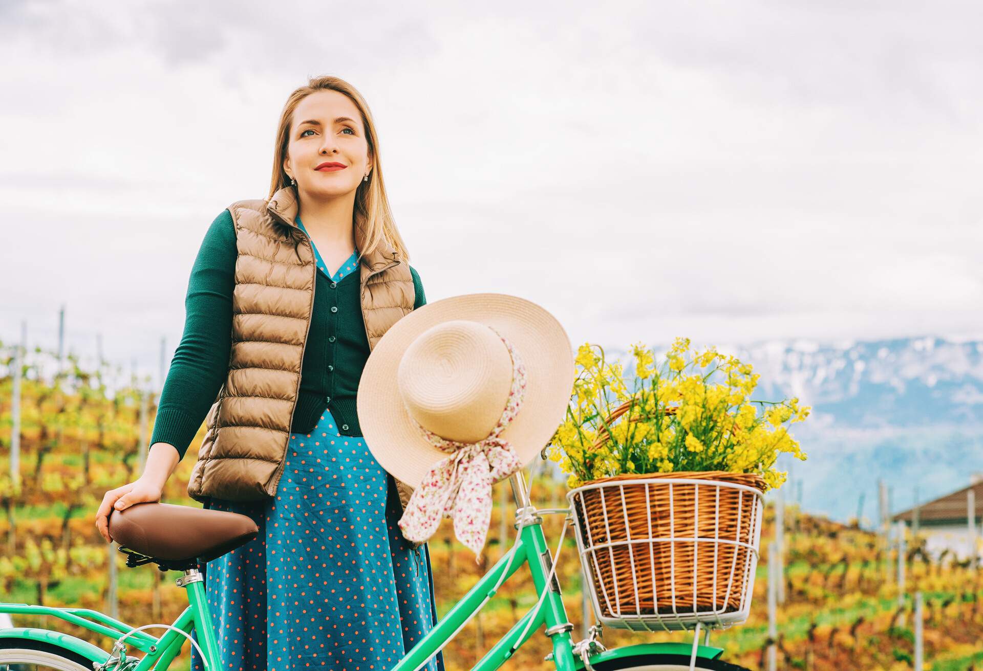 Retro styled portrait of beautiful young woman, wearing vintage clothes, holding mint color bicycle with yellow flowers placed in basket
