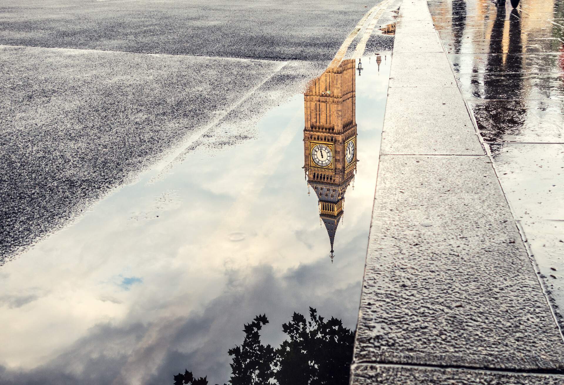 The Big Ben tower reflecting in a puddle along the sidewalk.