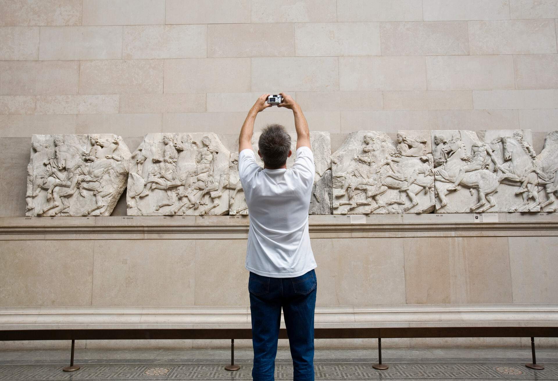 A man in a white shirt taking a photo of the bas-relief sculptures.