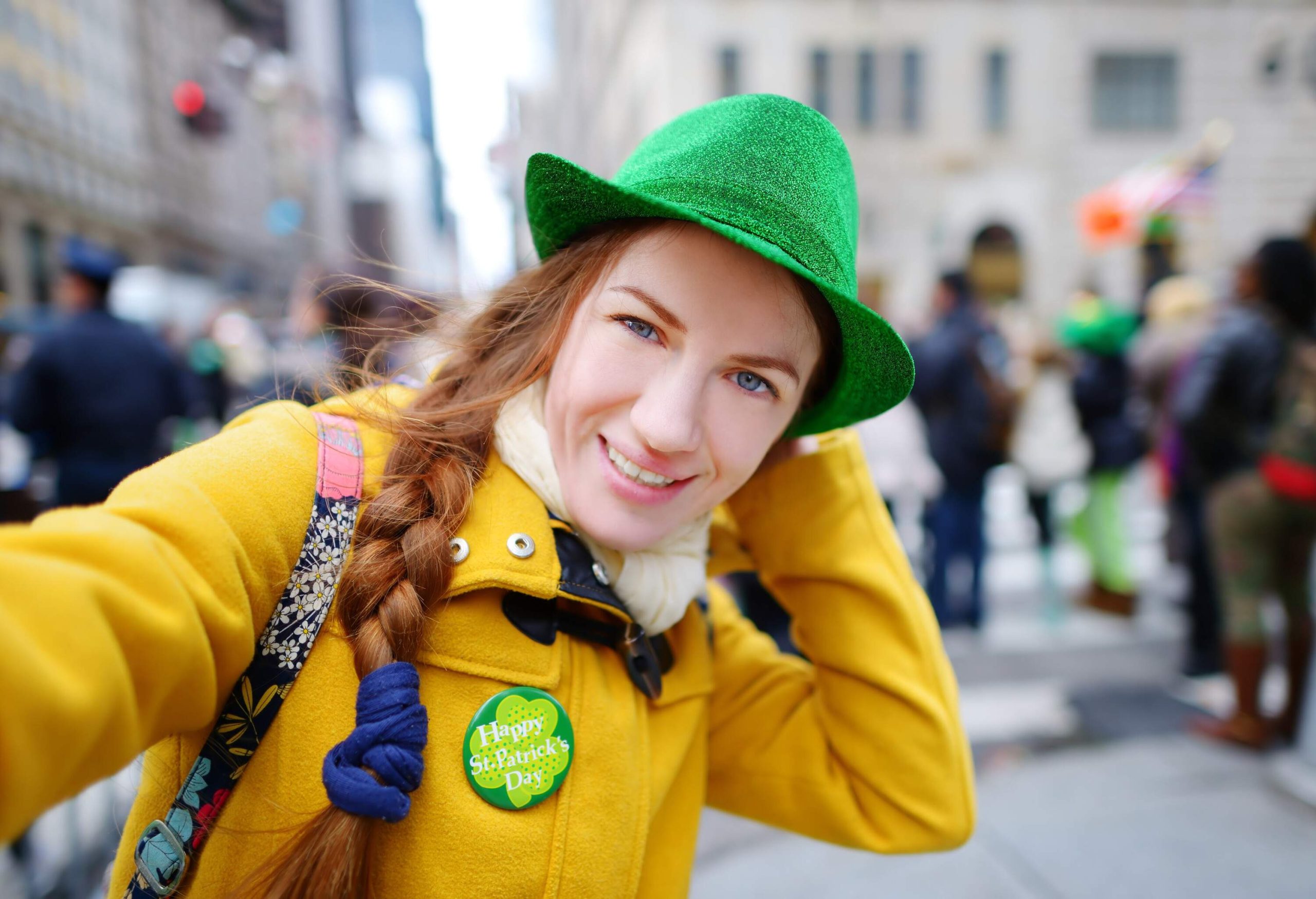 Portrait of a happy woman in a yellow jacket and green hat against the bokeh background of the crowd.