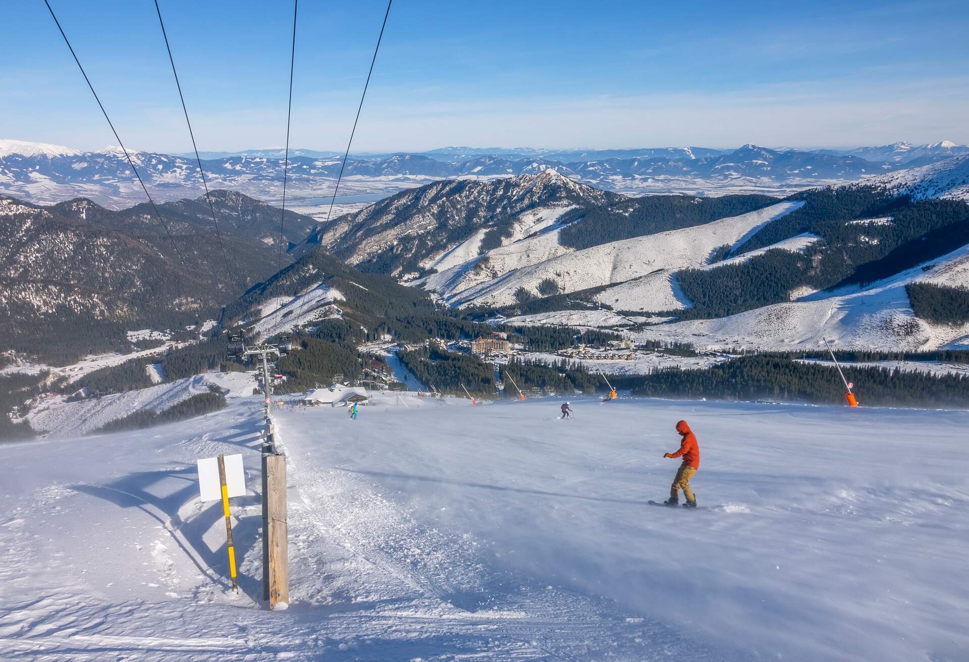 Snowboarders descending a snow slope with views of snowy mountains in the distance.