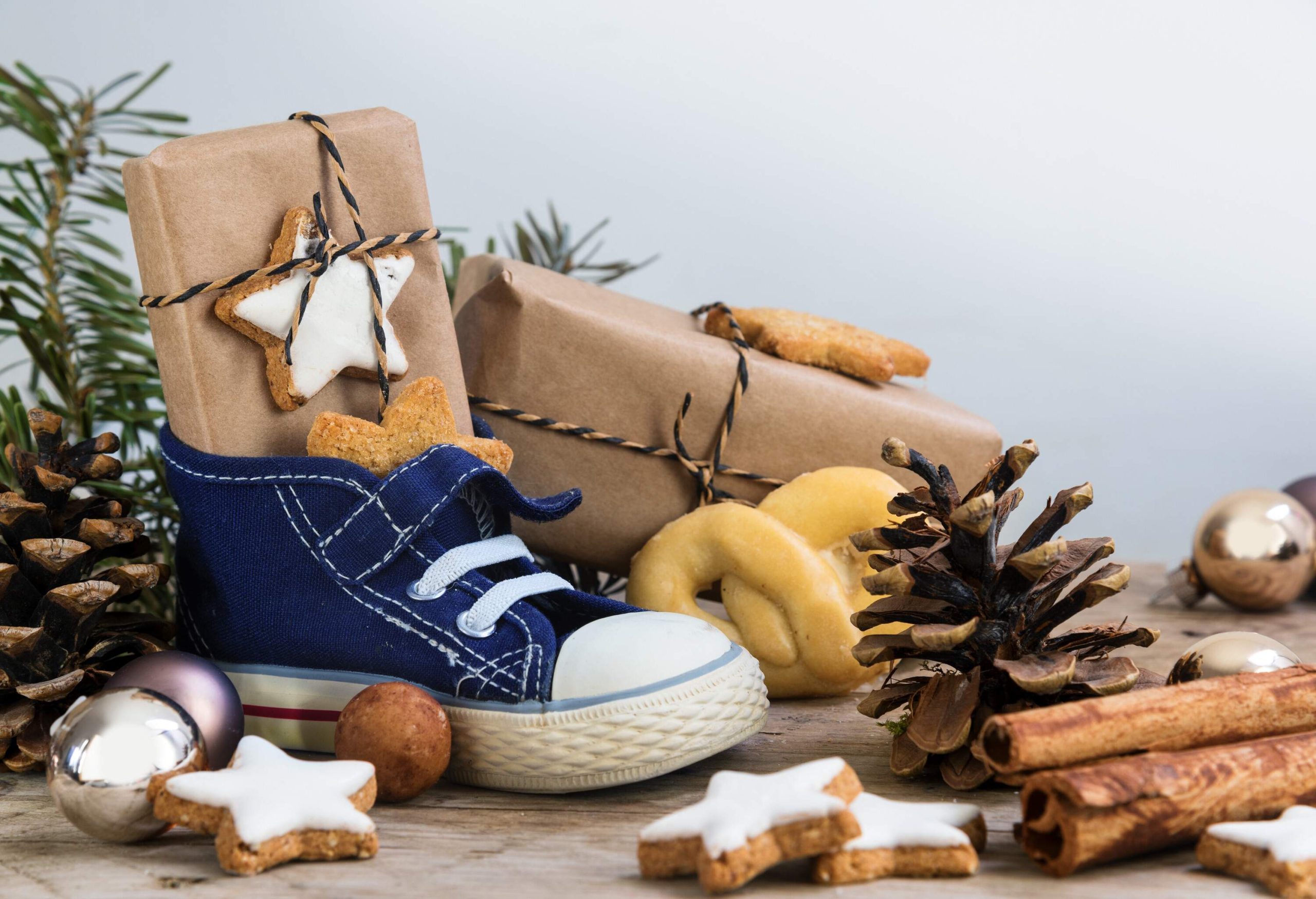 A clutter of a kid's shoe, gifts, cookies, and Christmas ornaments on wood. 