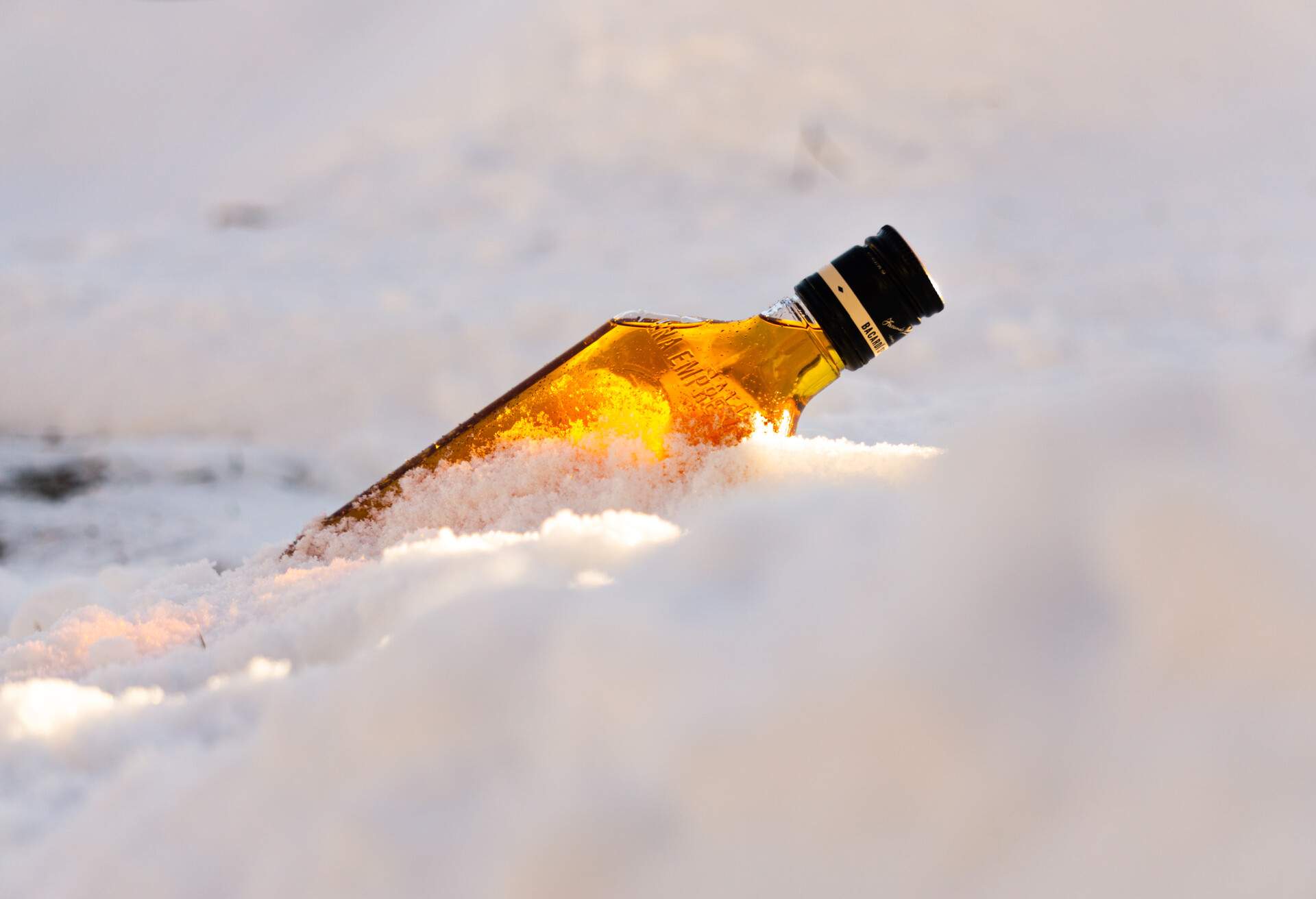 A beautiful day with a sunrise with a bottle of whiskey in a cold snow dune in the middle of winter