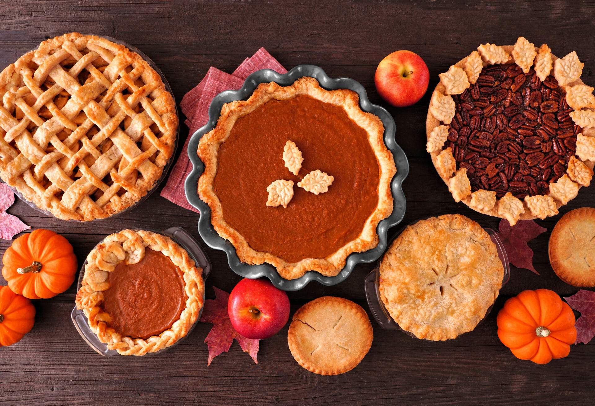 Assortment of homemade fall pies. Apple, pumpkin and pecan. Top down view table scene on a dark wood background.