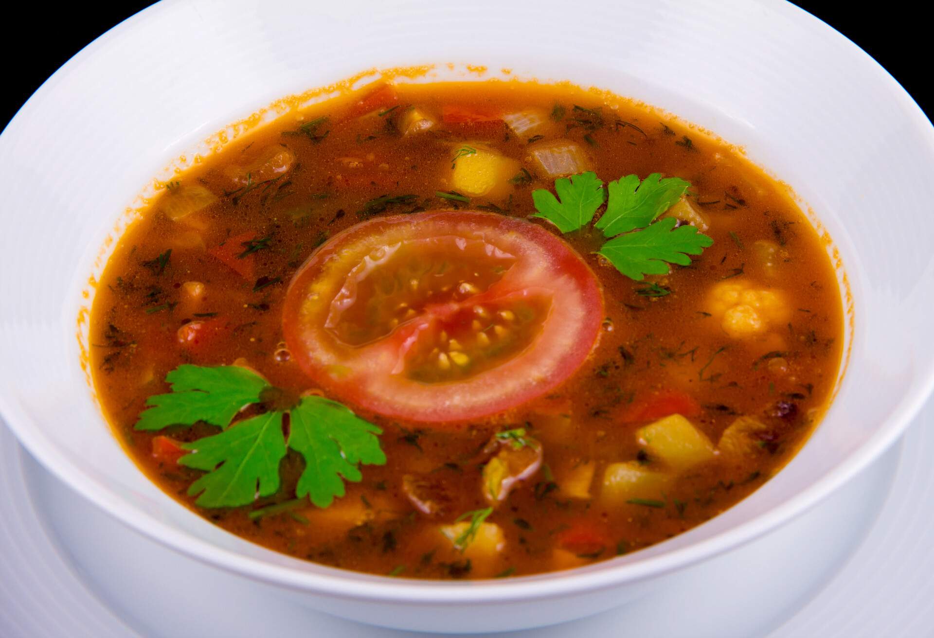 Hungarian goulash - thick vegetable soup with beef and tomatoes on white boul on black background.