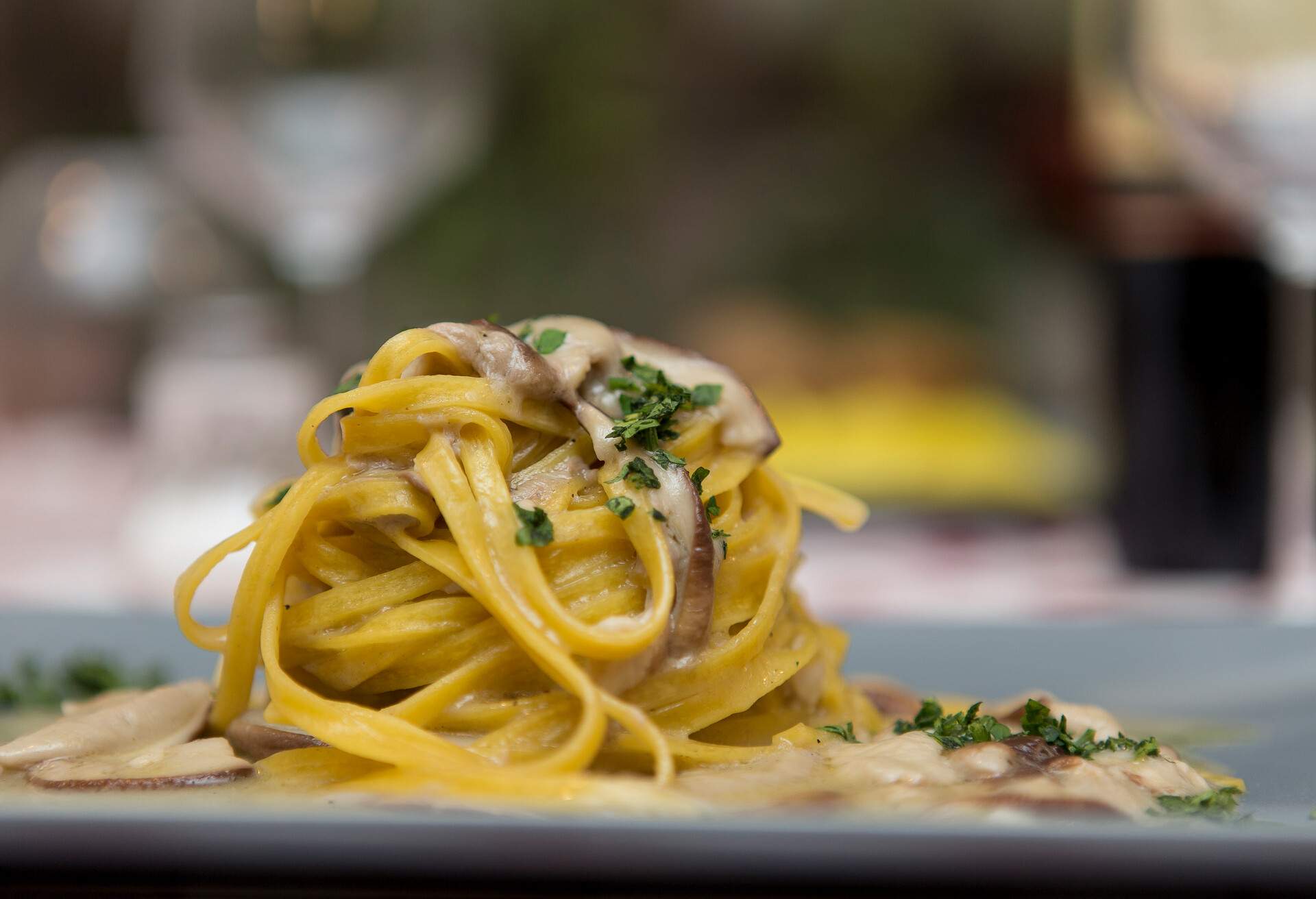 Close up on a restaurant table with a dish of italian pasta, tagliatelle with porcini mushrooms. Background is blurred, no people are visible in the frame.
