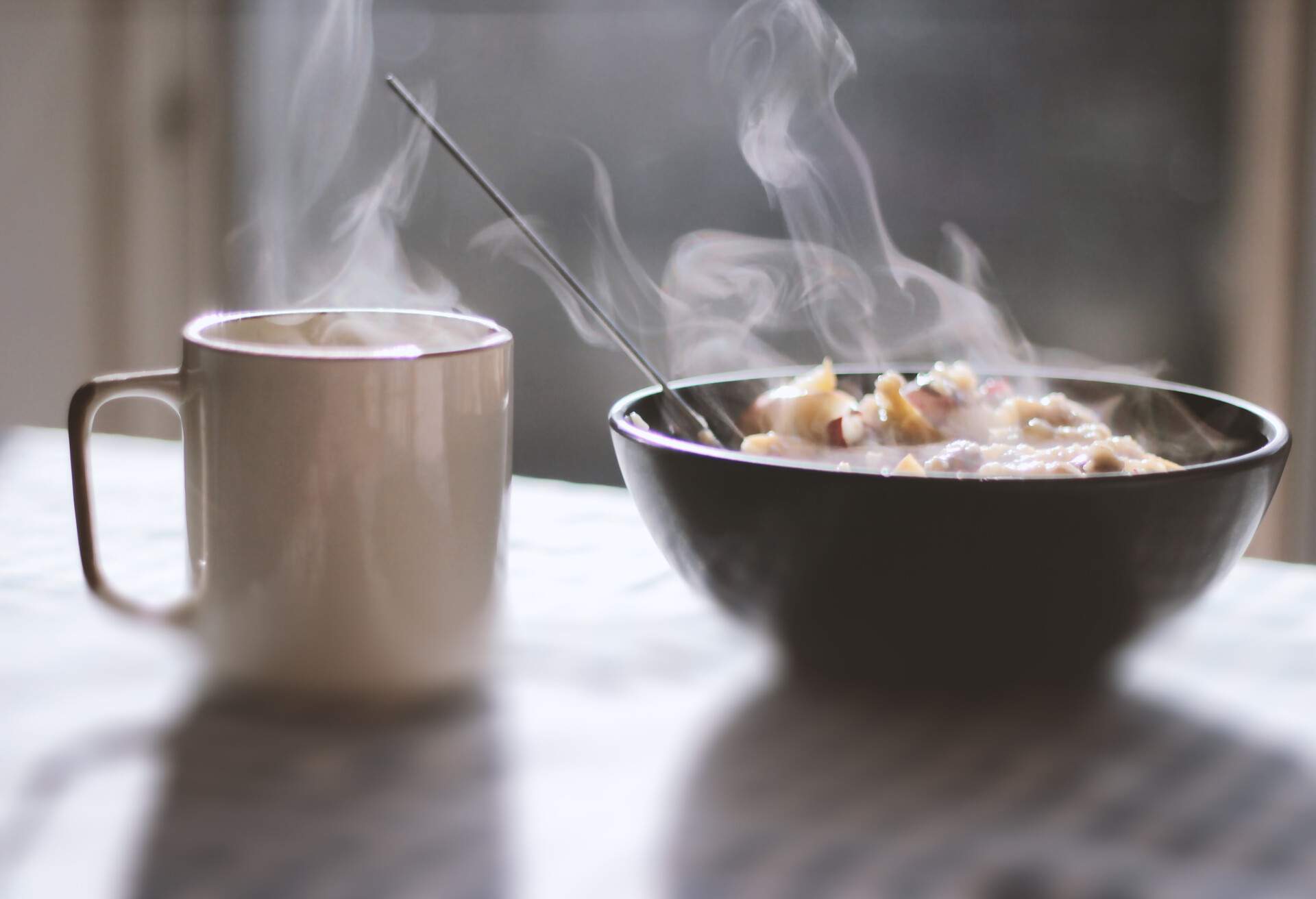 Close-up of porridge and tea served in a bowl on table with morning light and shadows coming through the window in the background.