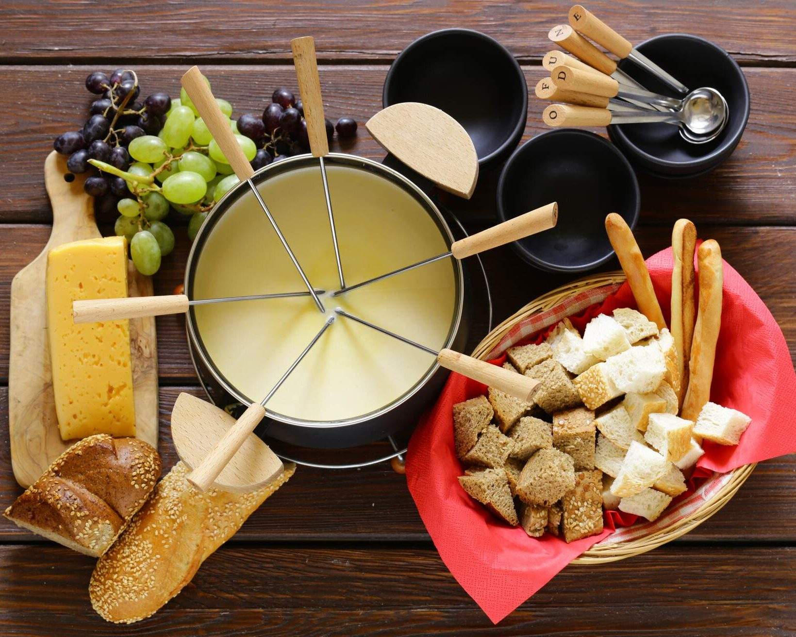 Traditional set of utensils for fondue, with bread, cheese, grapes