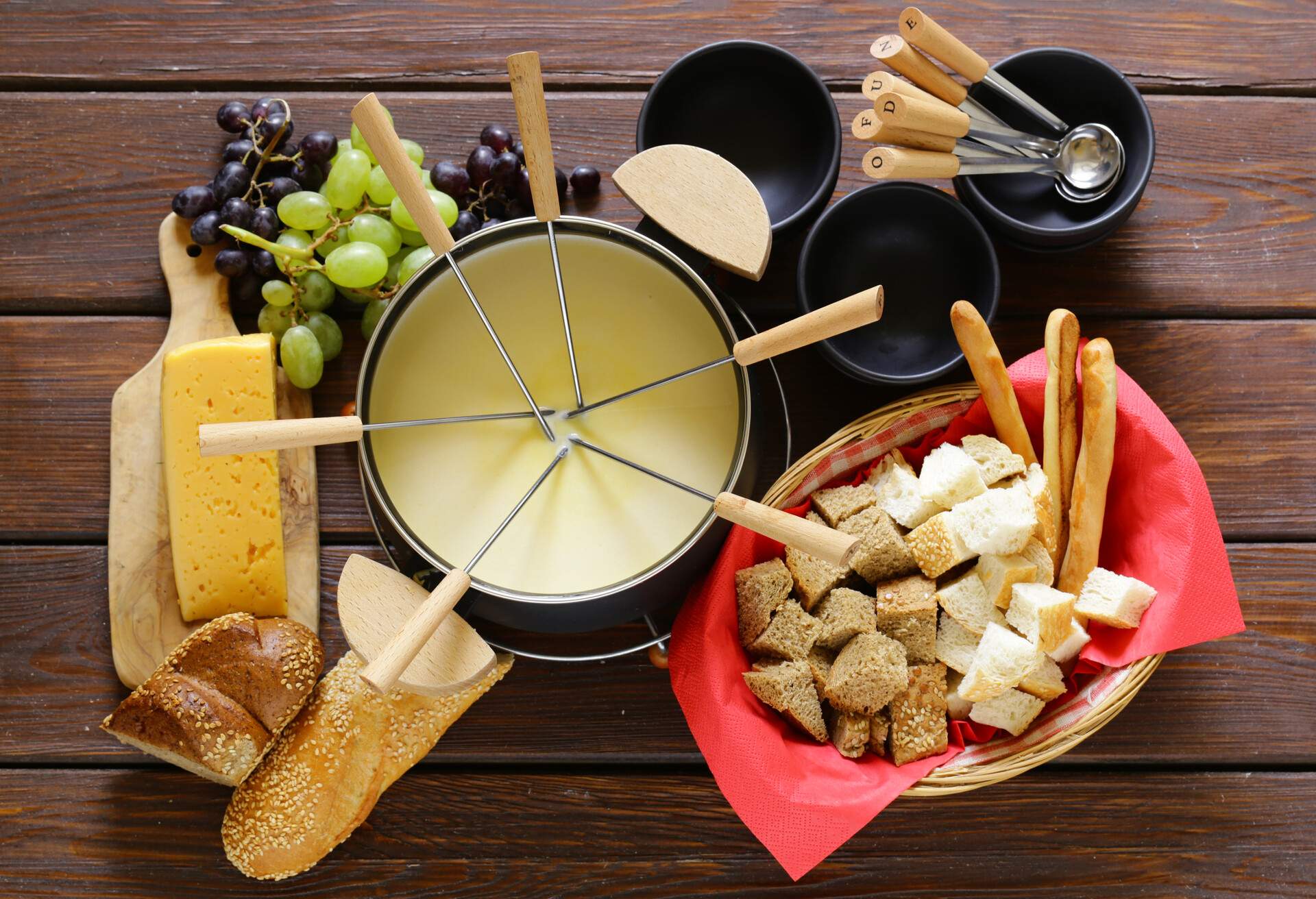 Traditional set of utensils for fondue, with bread, cheese, grapes