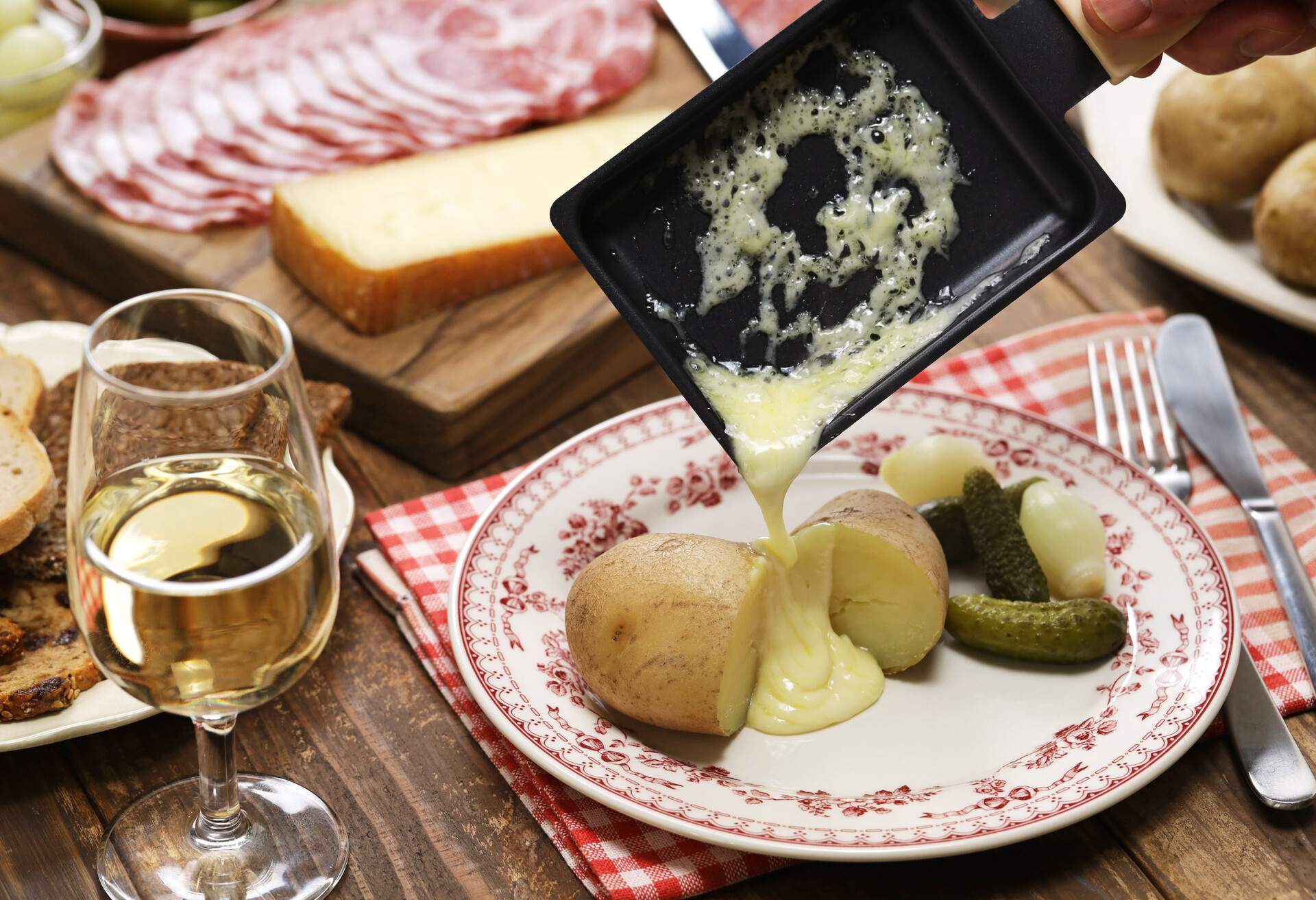 Raclette cheese melted by raclette pan is putting on freshly boiled potatoes.