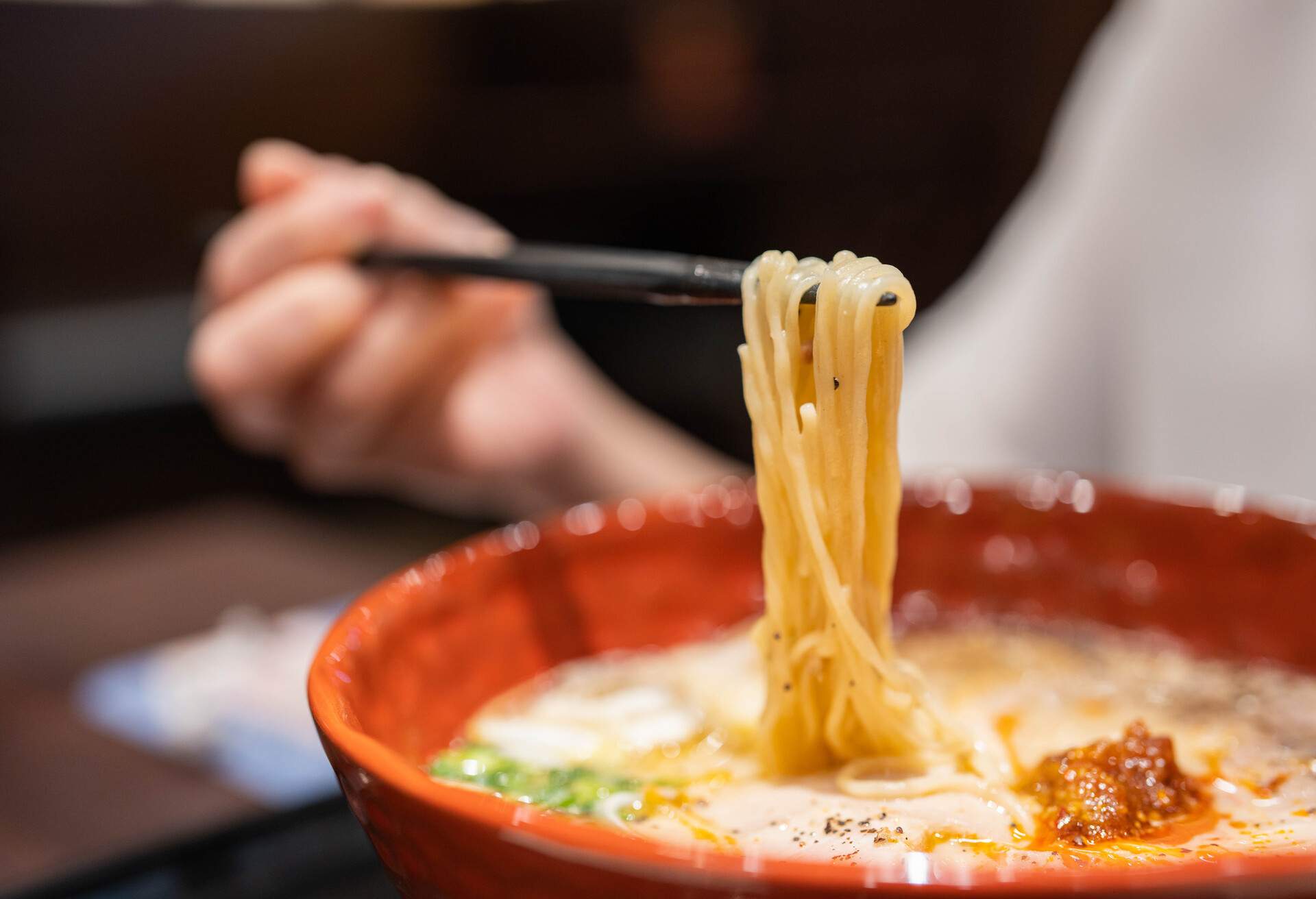 Ramen noodle lifted up by chopsticks with steam against restaurant background