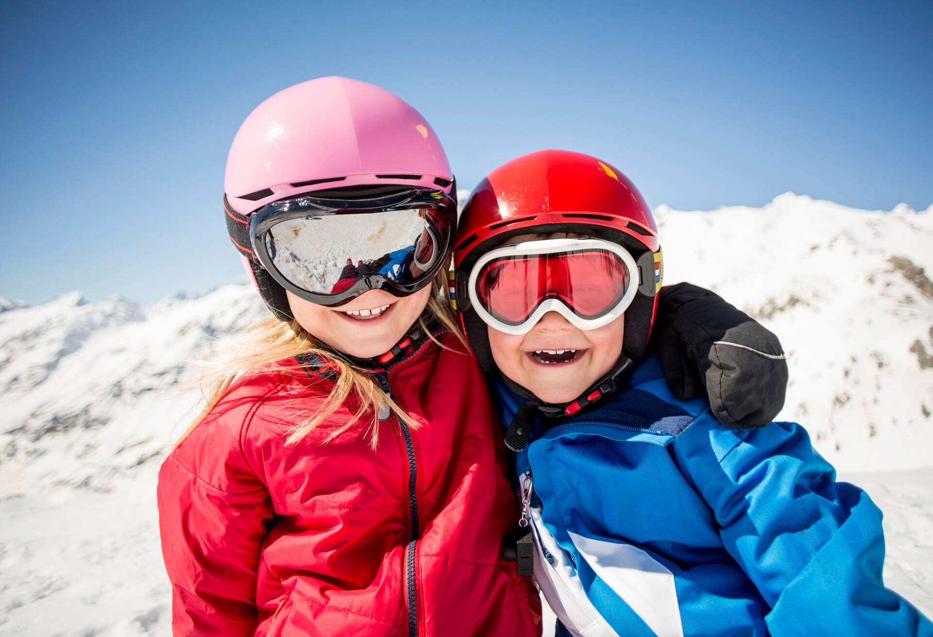 Two joyful kids wearing ski goggles and helmets standing on a snowfield.