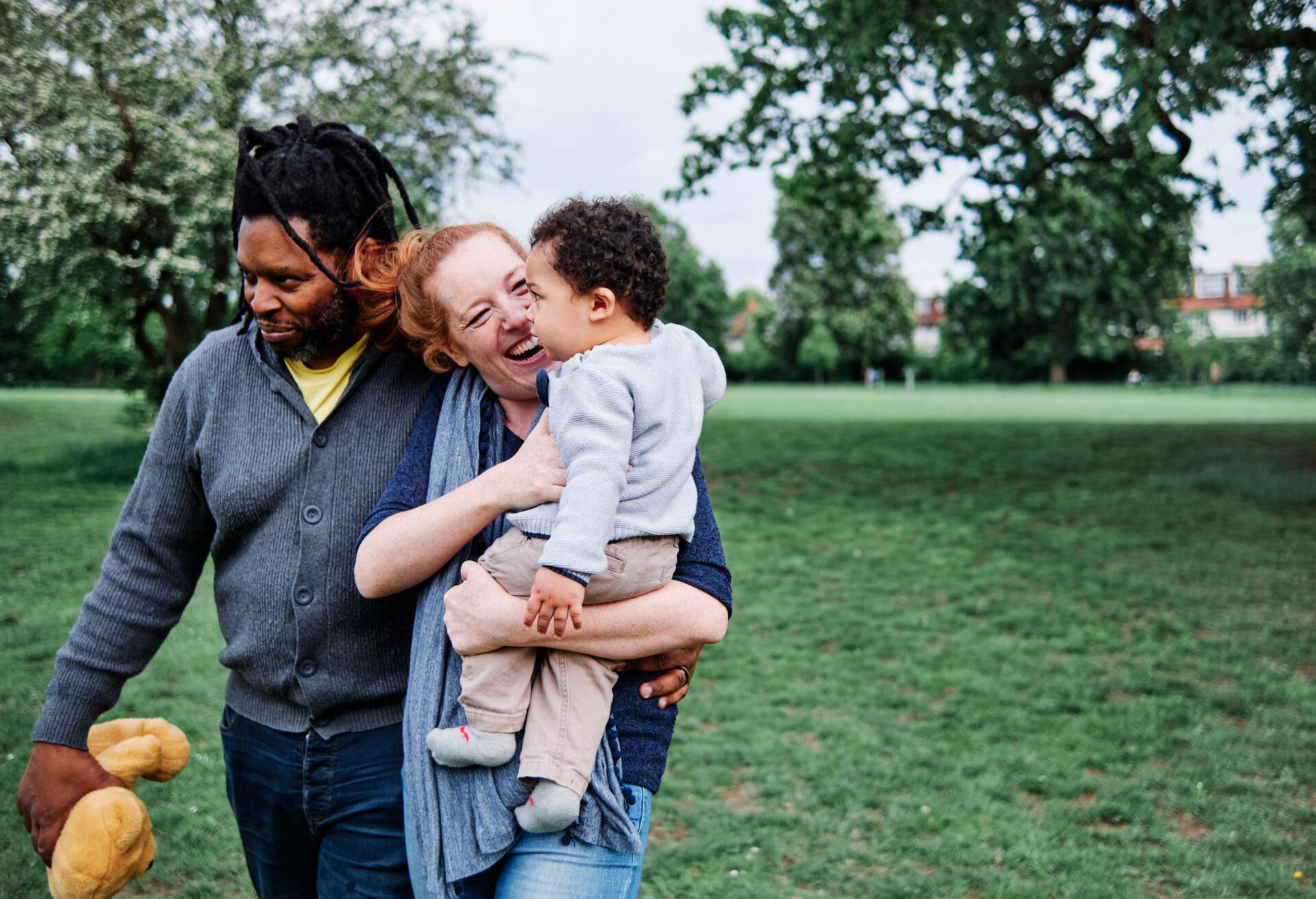 A smiling woman stands beside a man while carrying a baby.