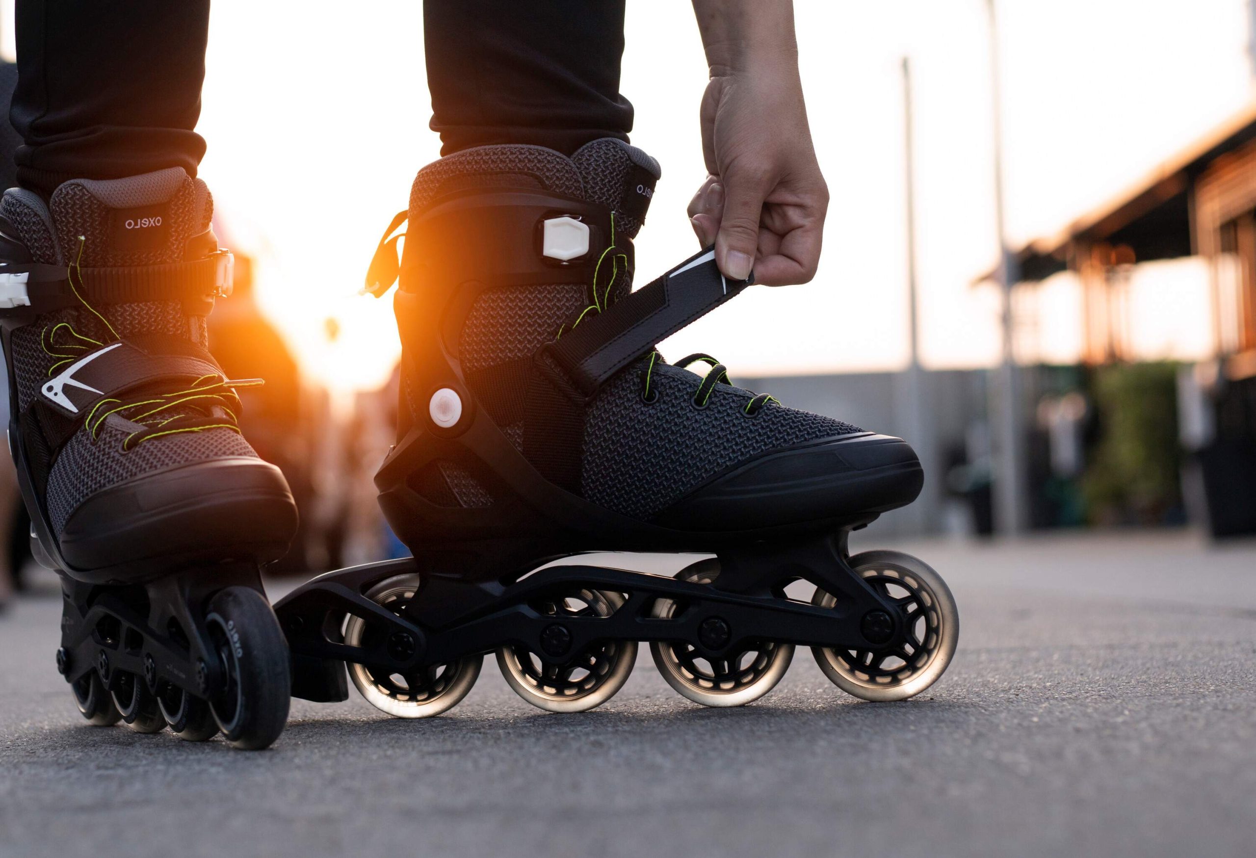 A hand fixes a roller blade's strap against the backdrop of a sunset.