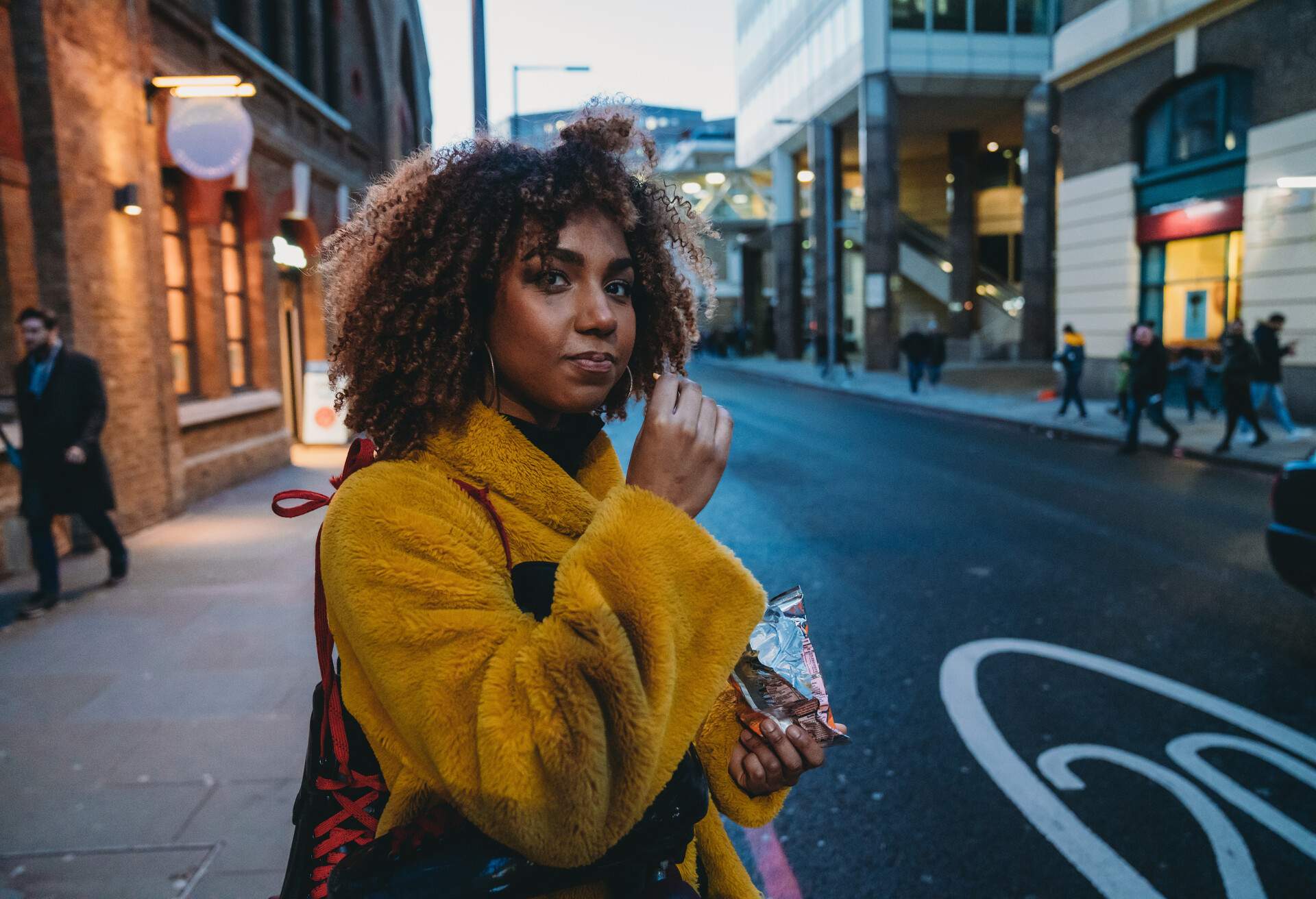 Hip young adult woman waiting for a ride in London. She's eating potato chips.