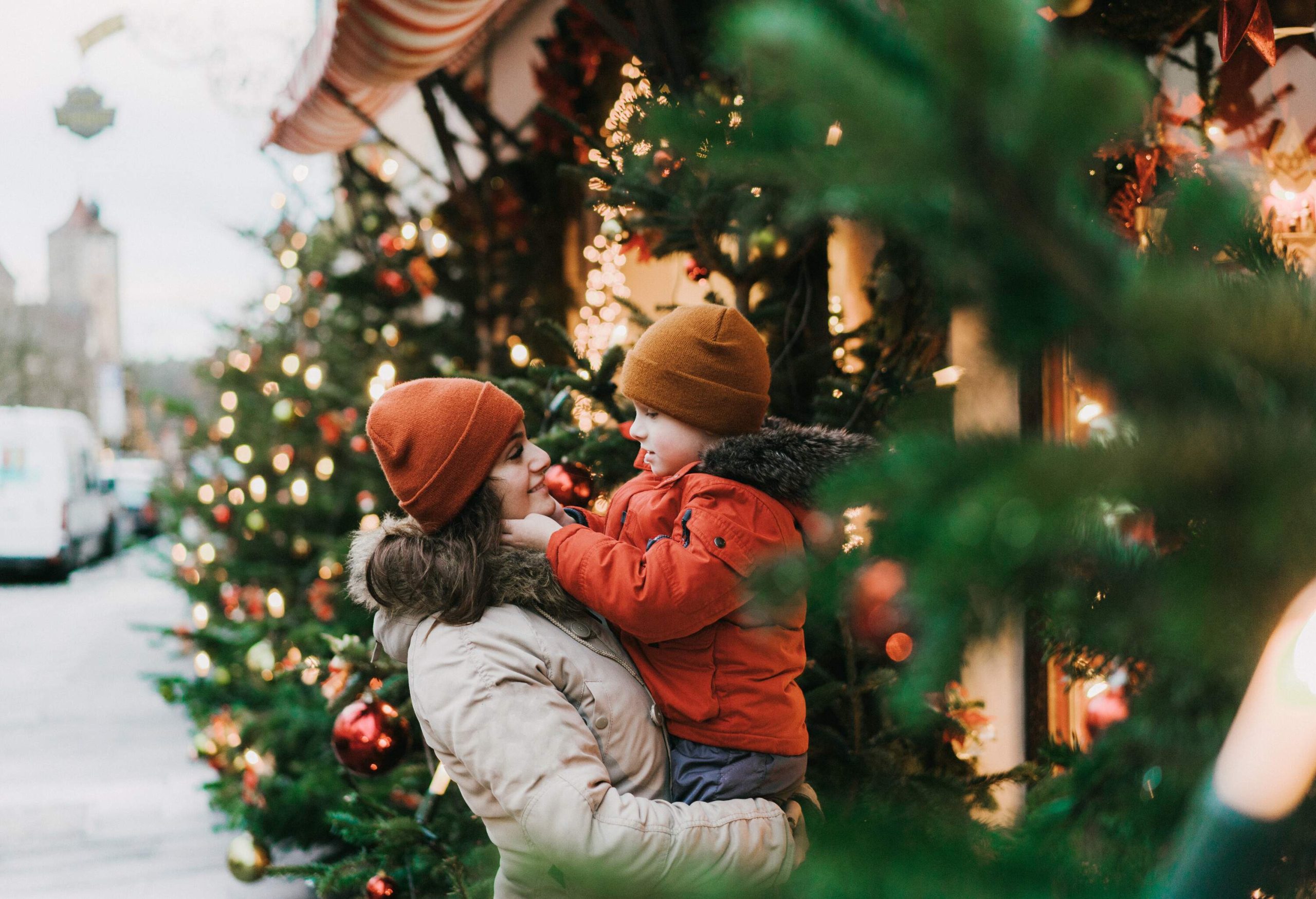 A mother and son in winter clothing standing next to a Christmas tree.