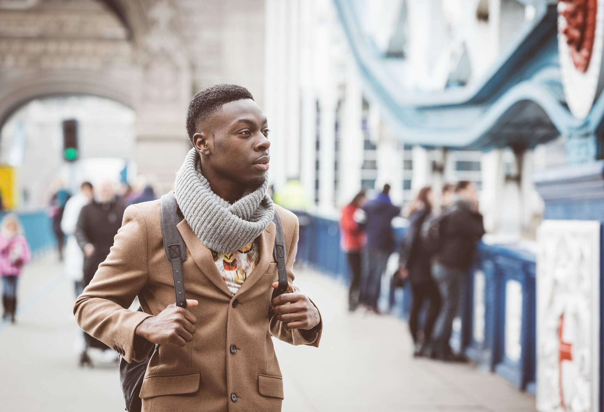 A young man in winter clothing in a bokeh background of people on a bridge.