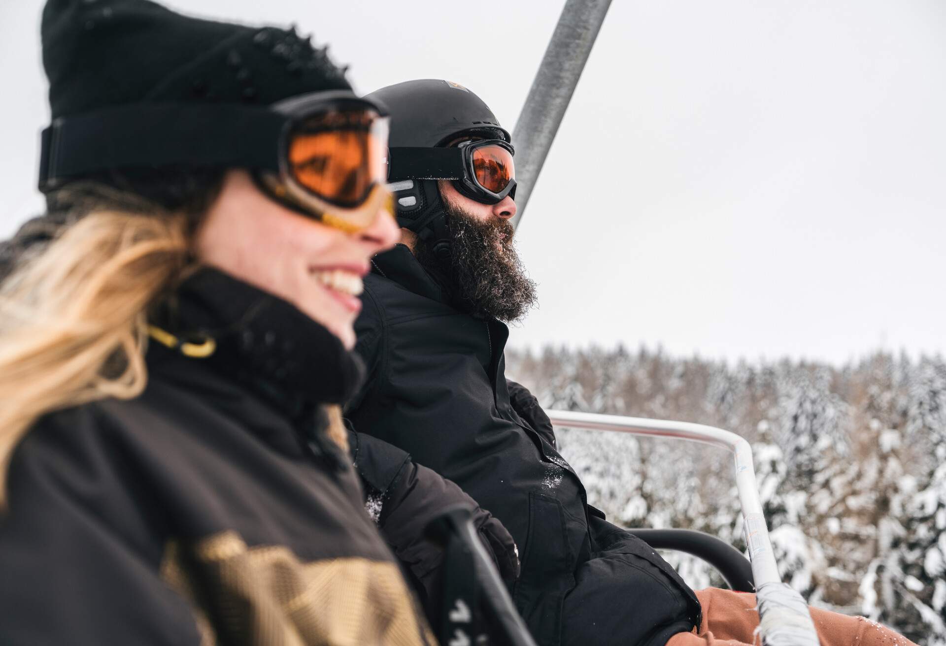 A couple on a chairlift overlooking the snow-covered trees below.