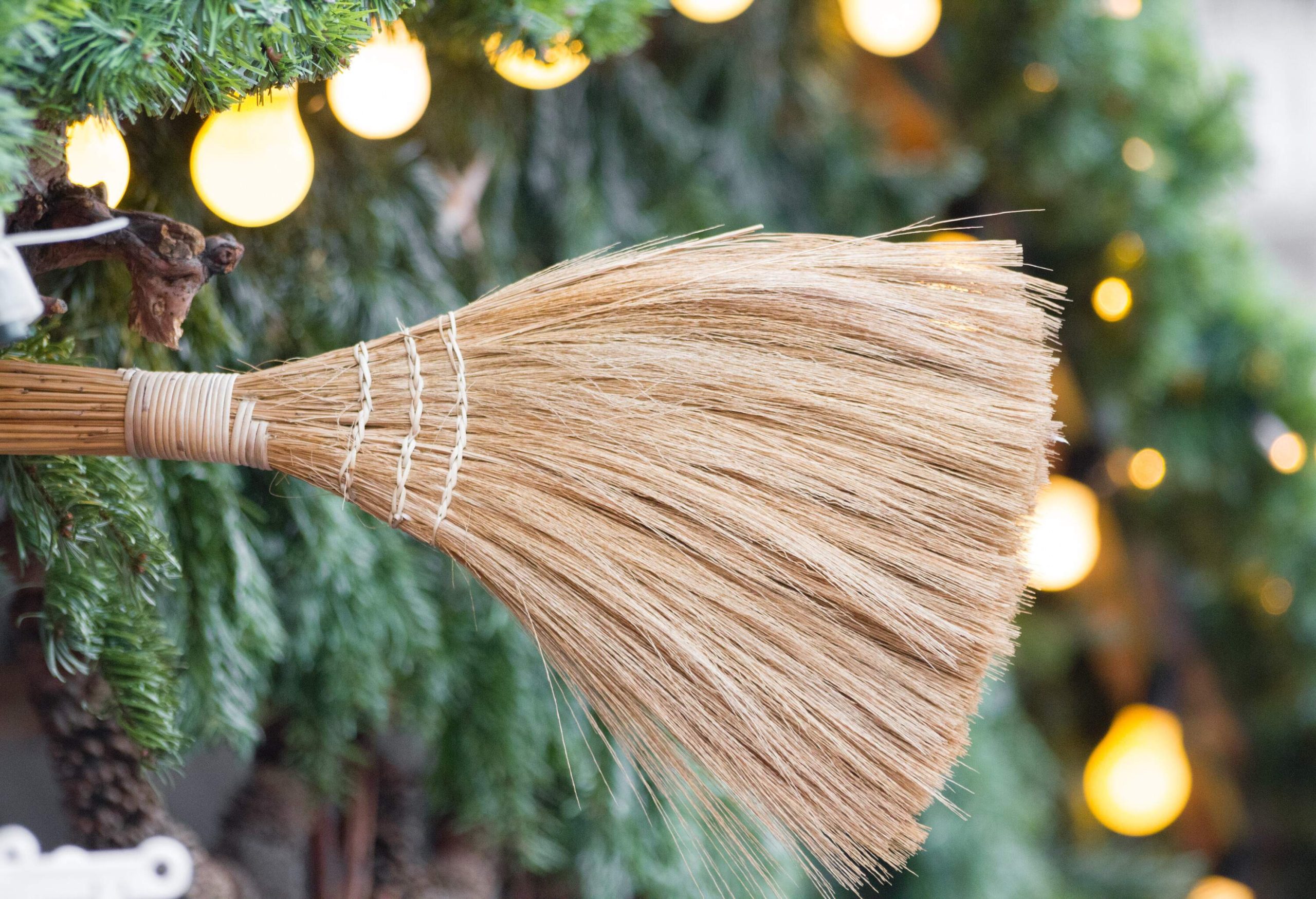 A broomstick sticking out from a background of pine needles and string lights.