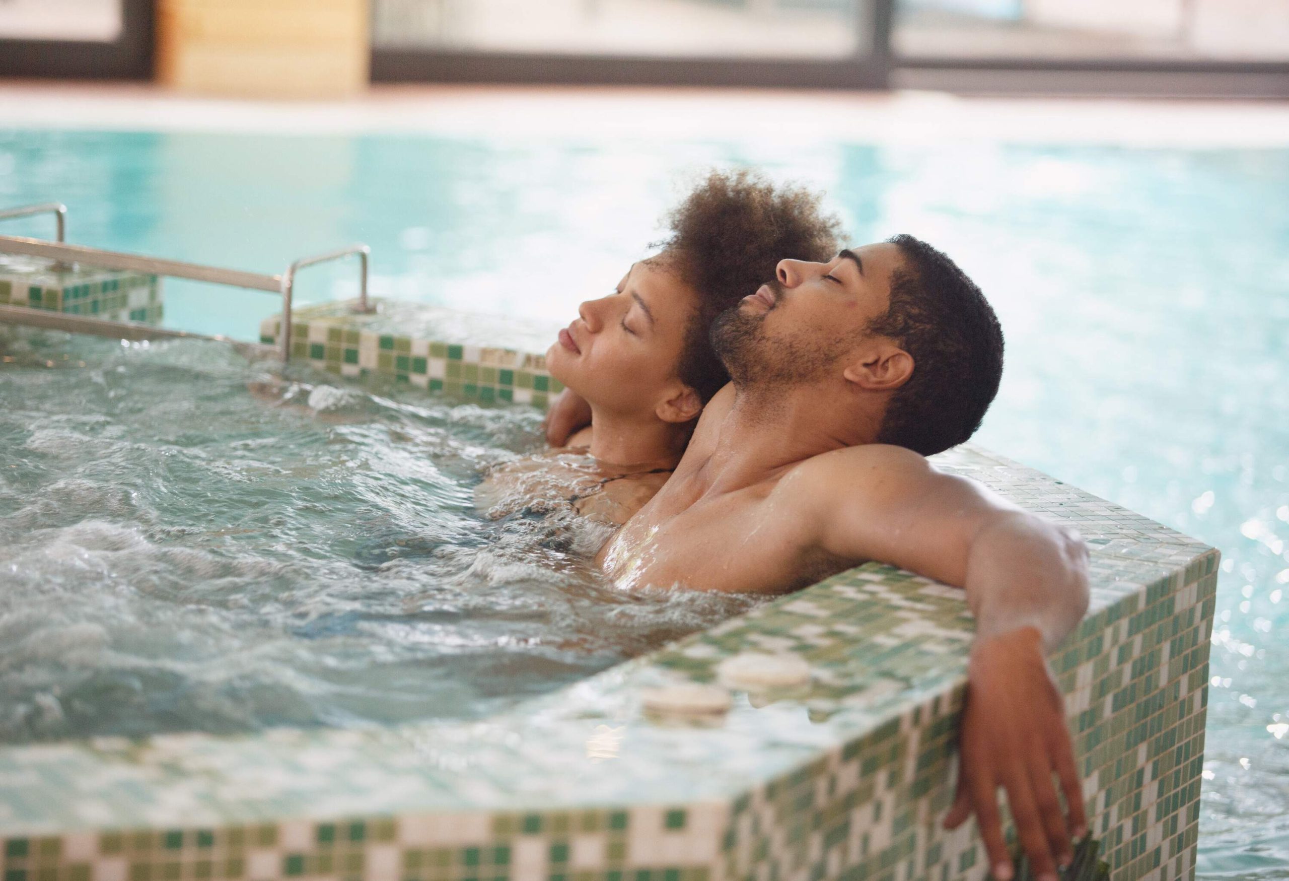A couple relaxes in a hot tub with their eyes closed.